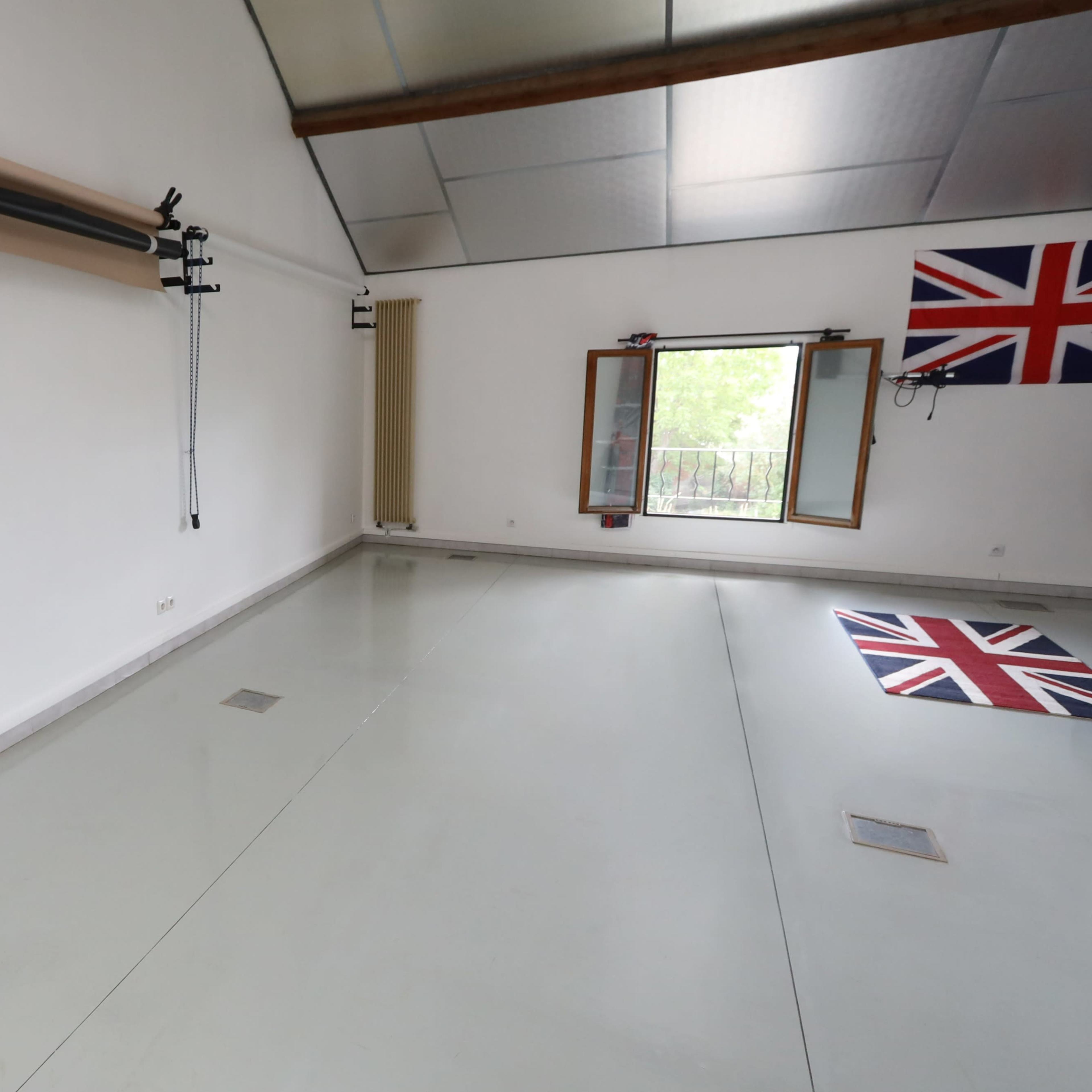 A spacious room with a white wall, gray flooring, and a large window, featuring a Union Jack flag on the floor and wall.