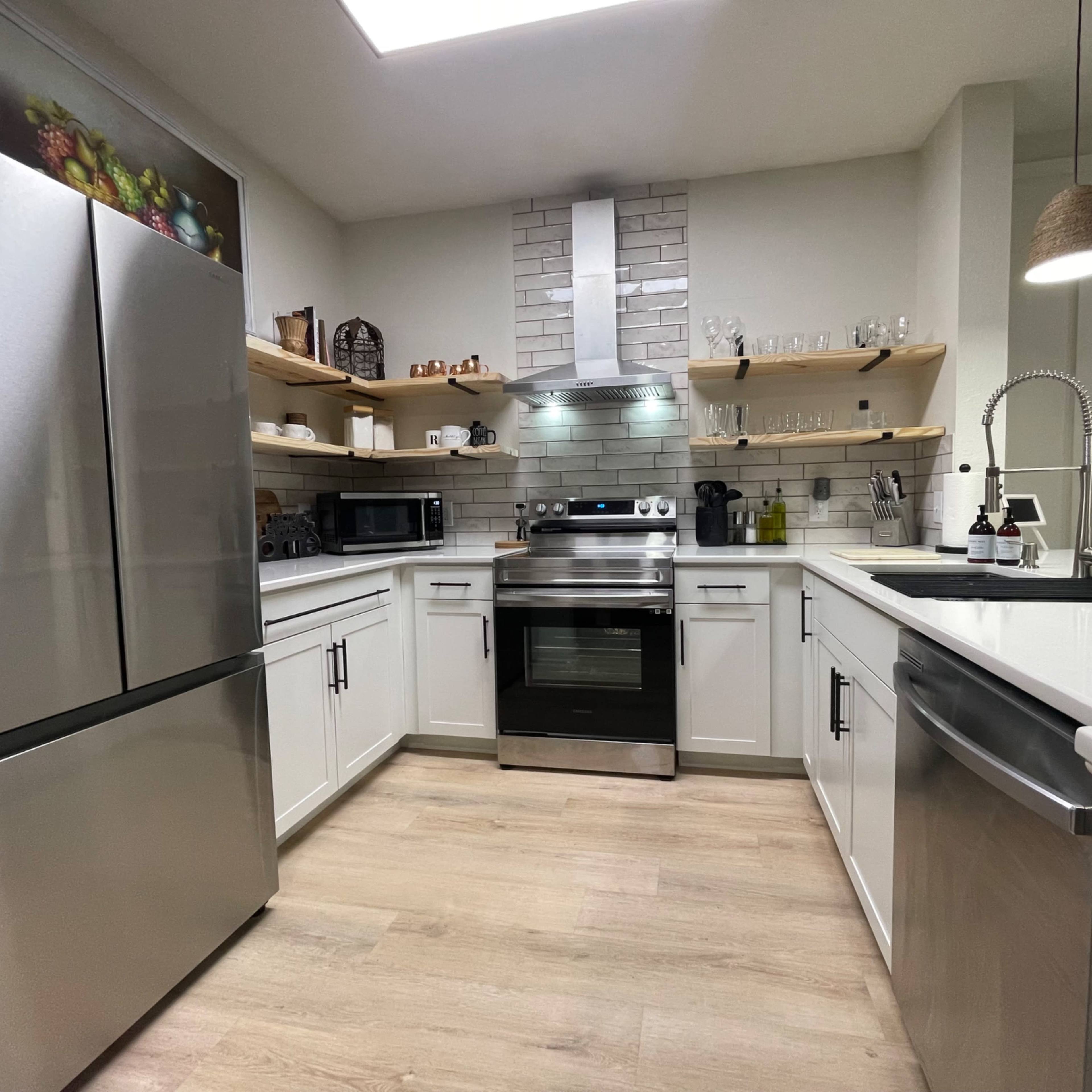 The kitchen features stainless steel appliances, white cabinets, and wooden shelving, creating a modern and organized space.