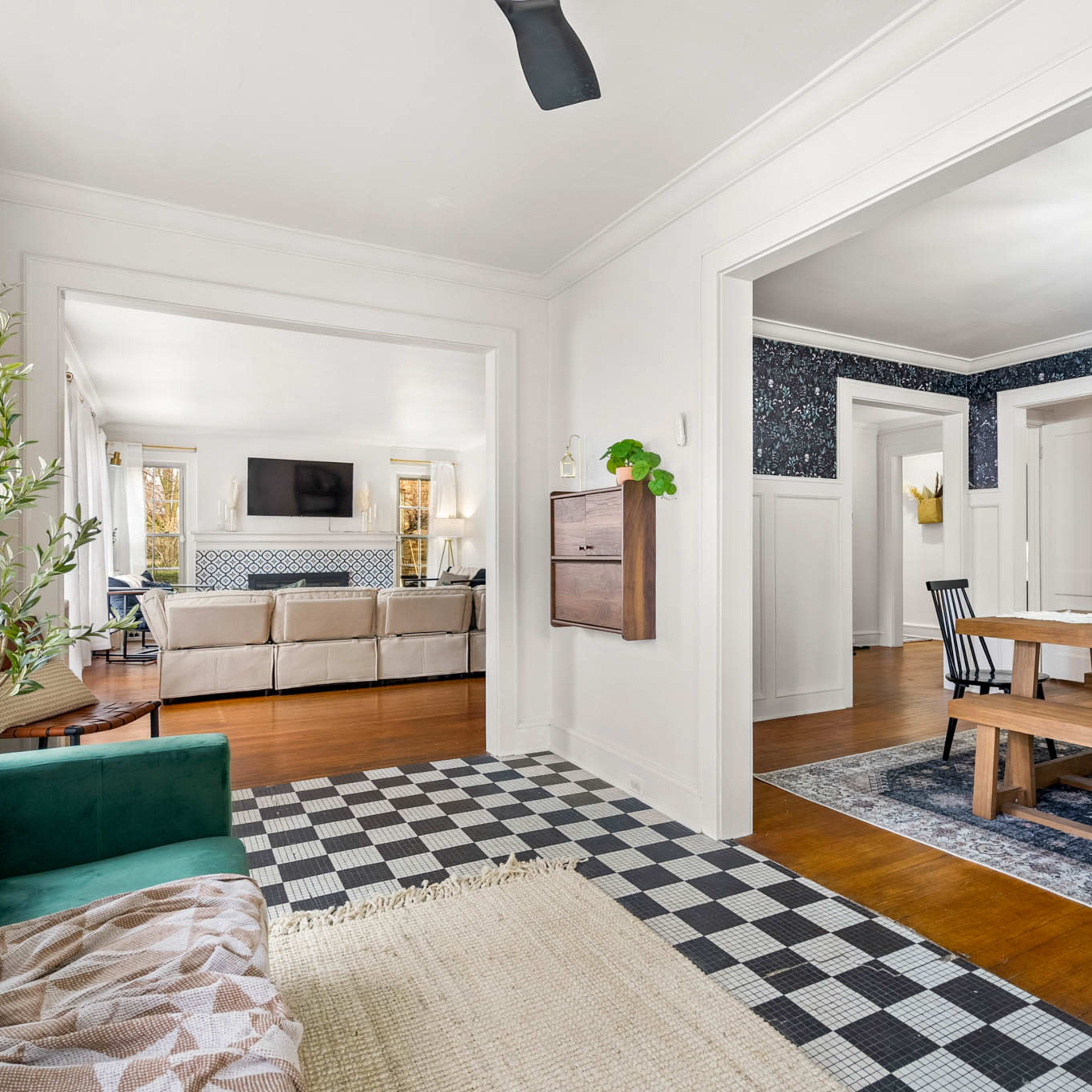 A foyer leading to an open living area, featuring a dining table and a cozy seating arrangement with a checkered floor and decorative elements.