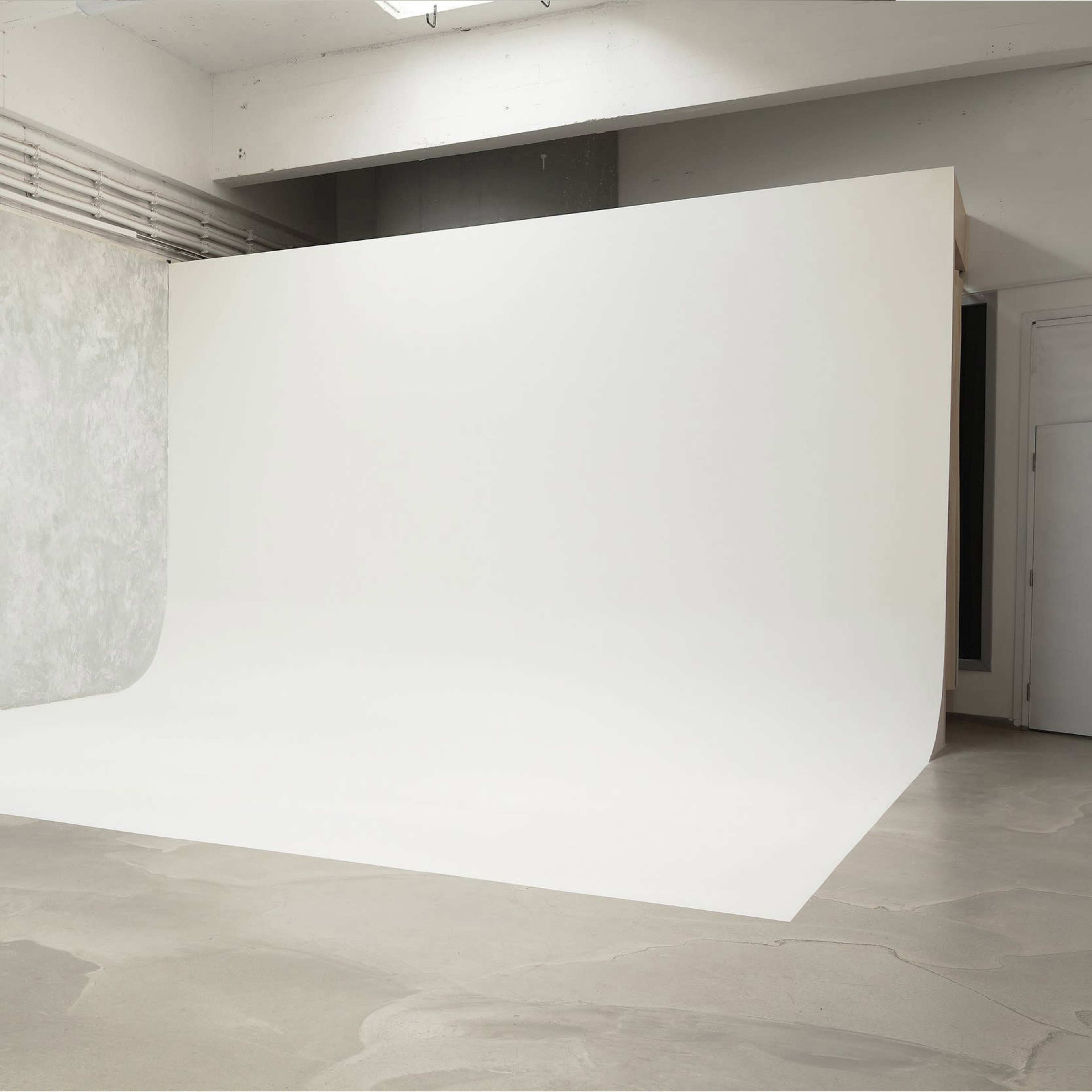 A spacious photo studio with a seamless white backdrop and a textured gray wall.