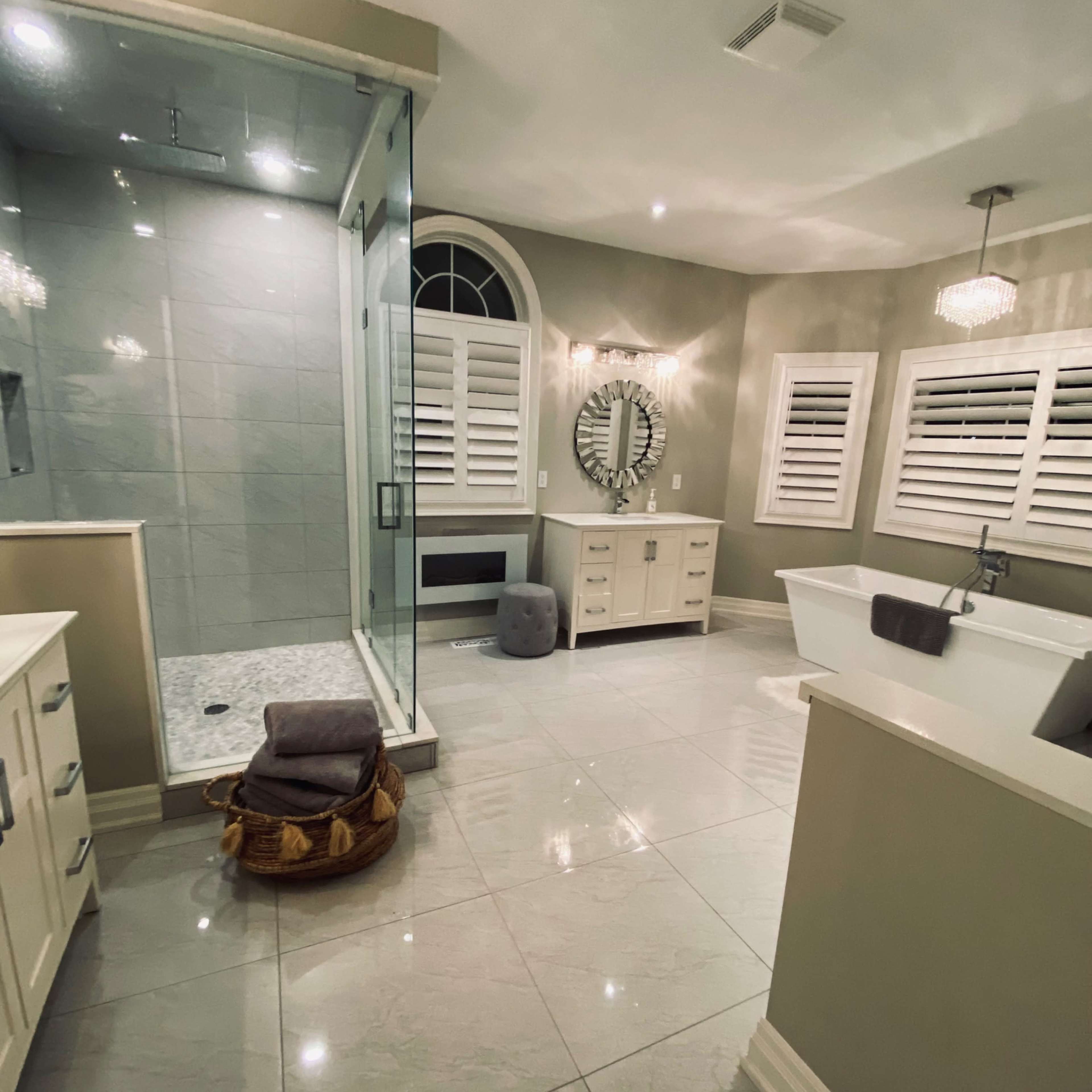 A modern bathroom featuring a glass-enclosed shower, a freestanding bathtub, and dual vanities, all set against sleek gray tile flooring and illuminated by pendant lights.