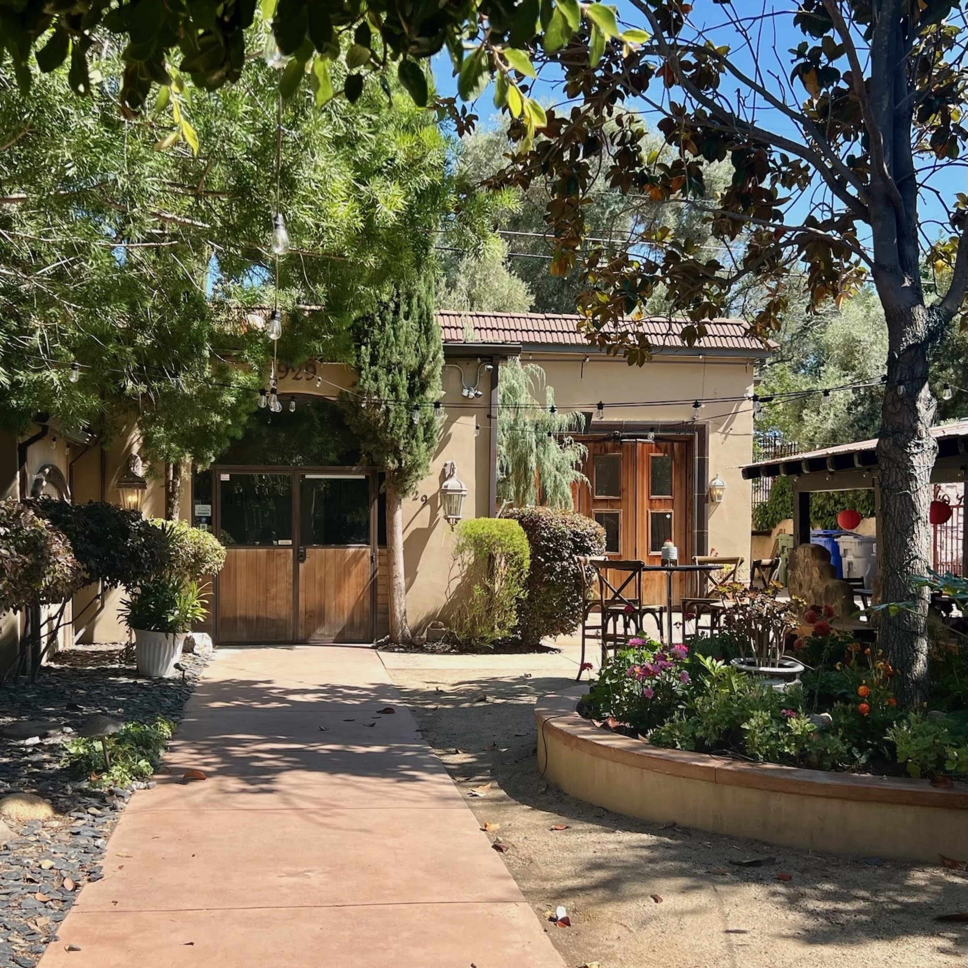 A pathway leads to a house surrounded by trees and garden areas with outdoor seating.