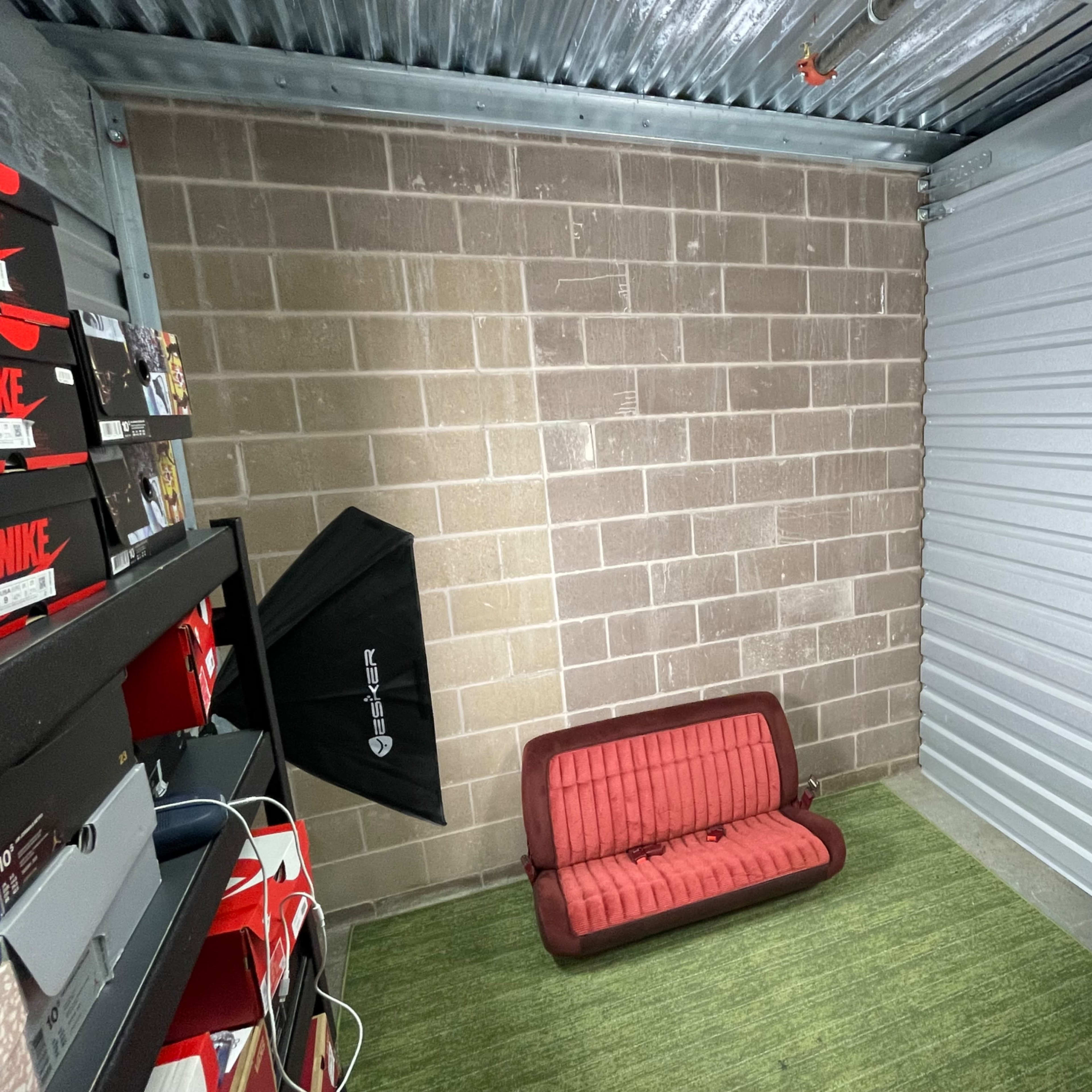 A small storage unit with a red couch, two softbox lights, and organized shoe boxes stacked on shelves against the wall.