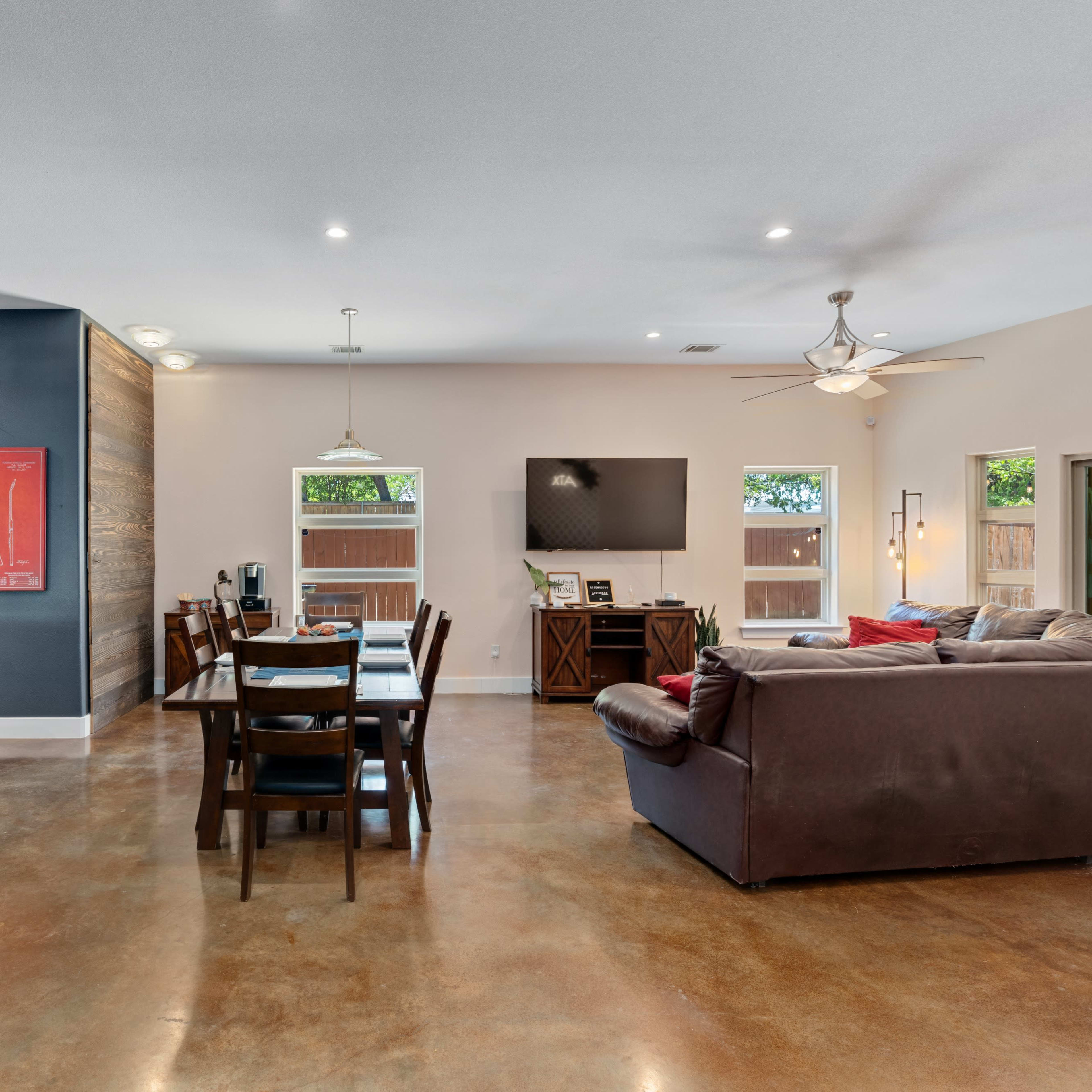 A spacious living and dining area featuring a wooden dining table, a dark sofa, and a kitchen bar with stools.