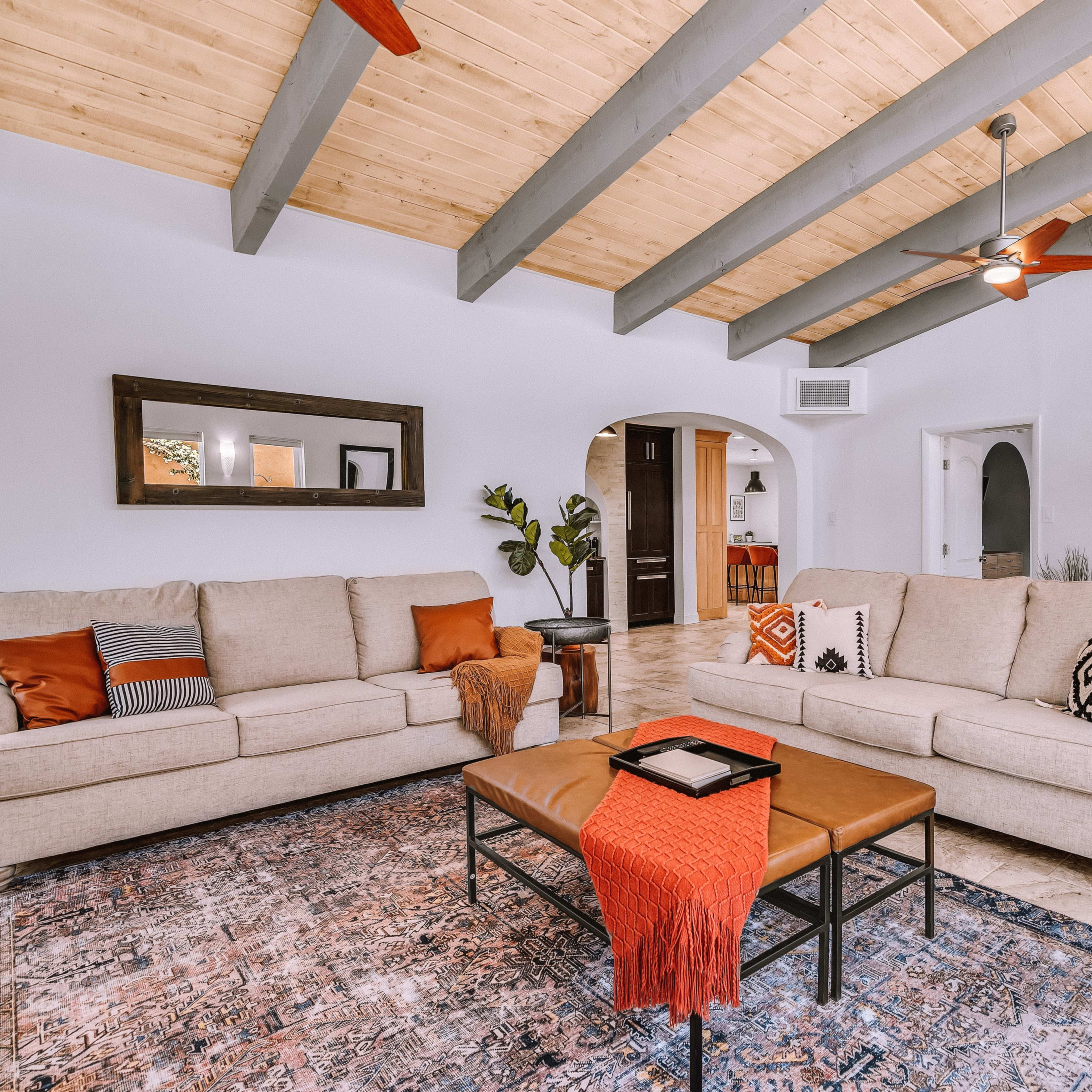 A cozy living room with two sofas facing a wooden coffee table, featuring a patterned rug and exposed beam ceiling.
