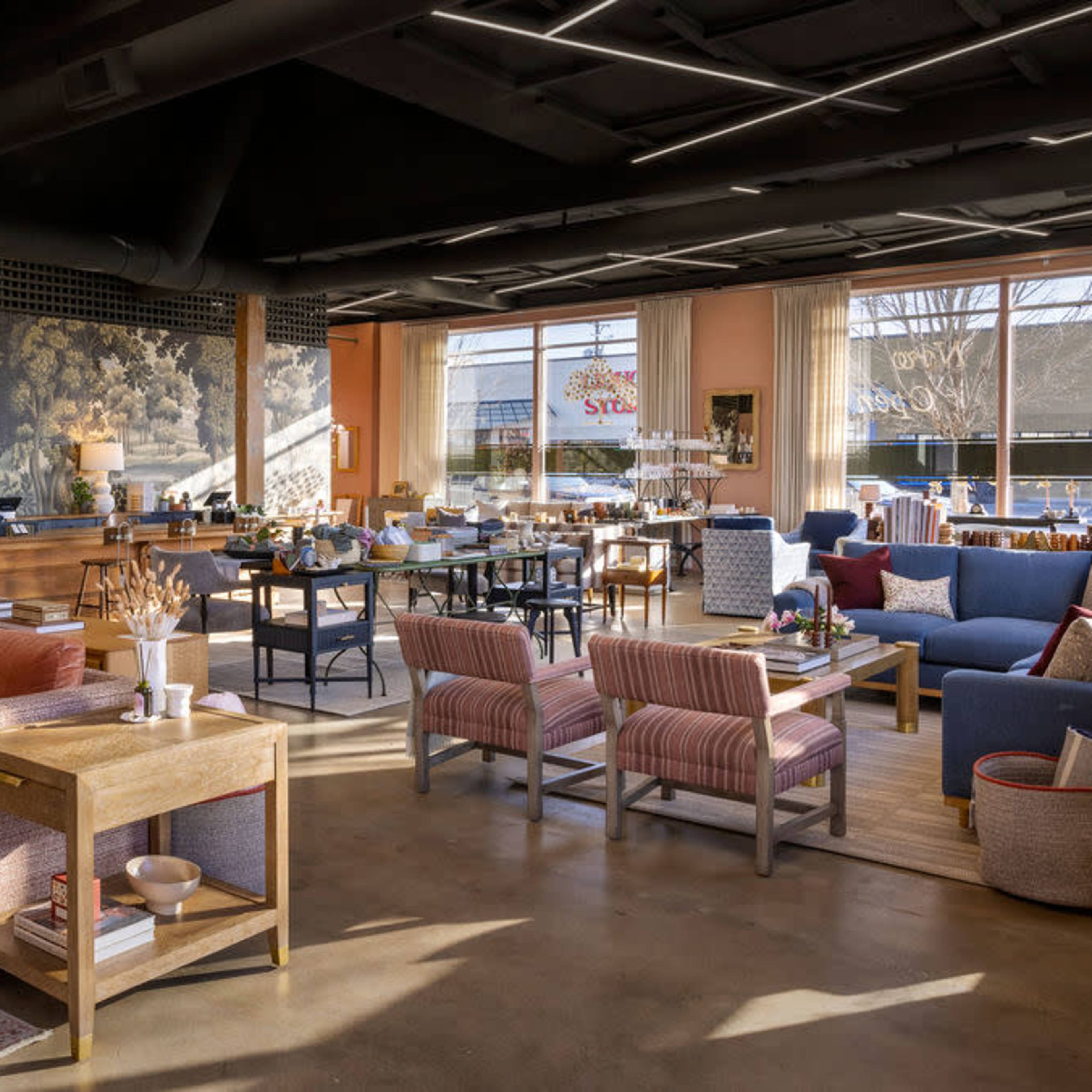 A spacious living area with a mix of seating including a large sectional sofa, various armchairs, and a dining table, all set against a backdrop of large windows and decorative wall art.