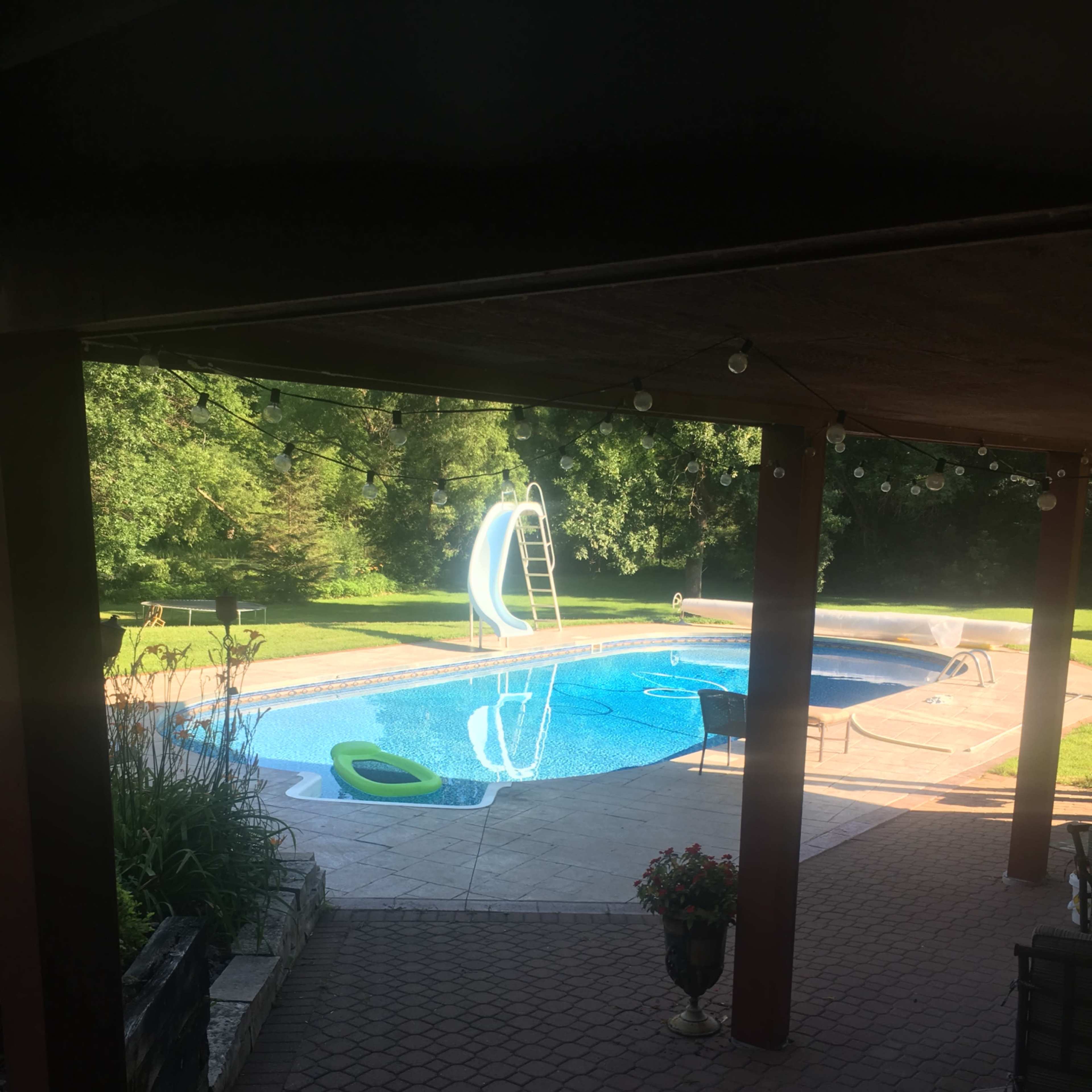A swimming pool with a slide is surrounded by greenery and a patio area with seating.