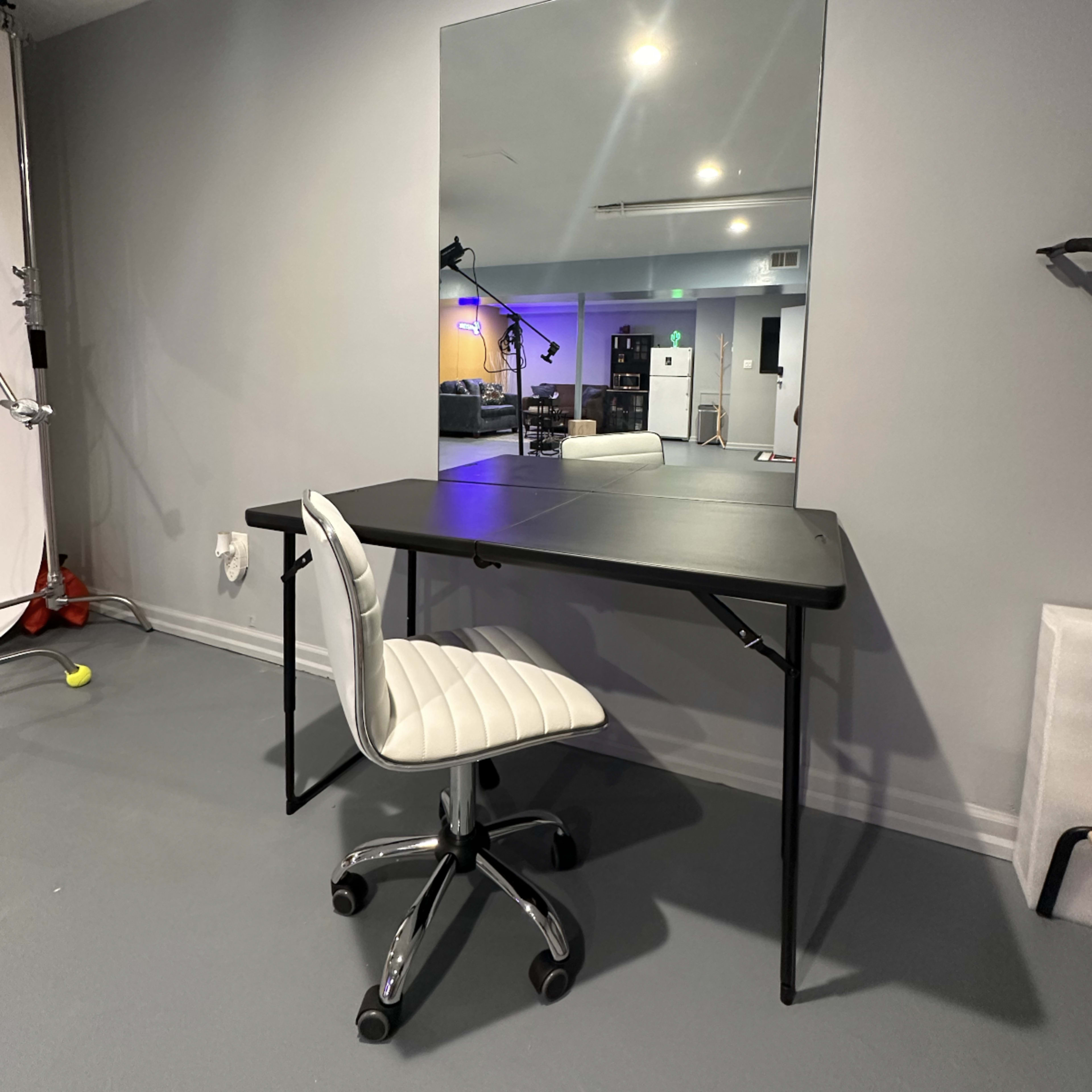 A black folding table with a matching swivel chair is positioned against a gray wall, reflecting a large mirror.