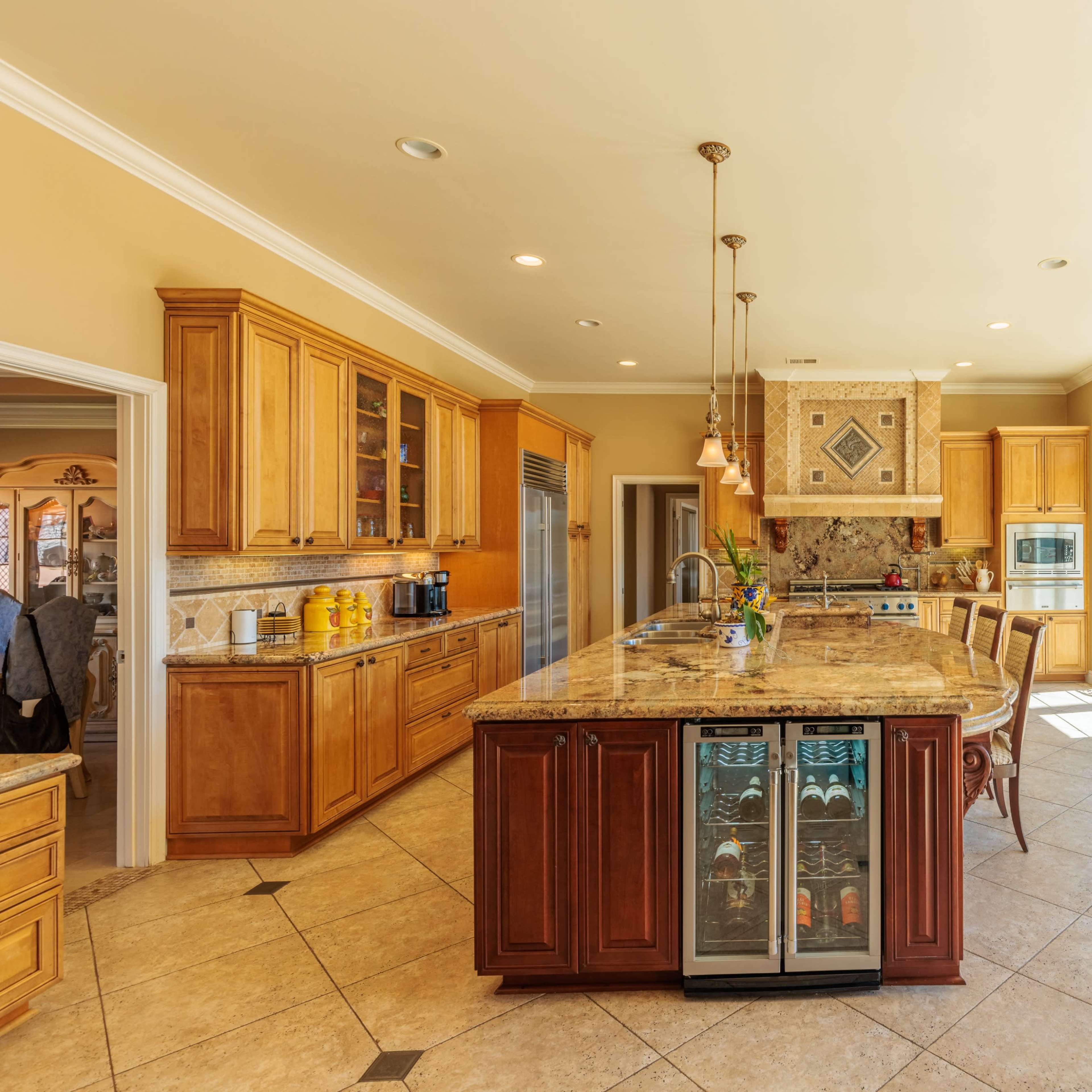A spacious kitchen with wooden cabinetry, a large central island, a wine fridge, and panoramic windows that open to an outdoor area.