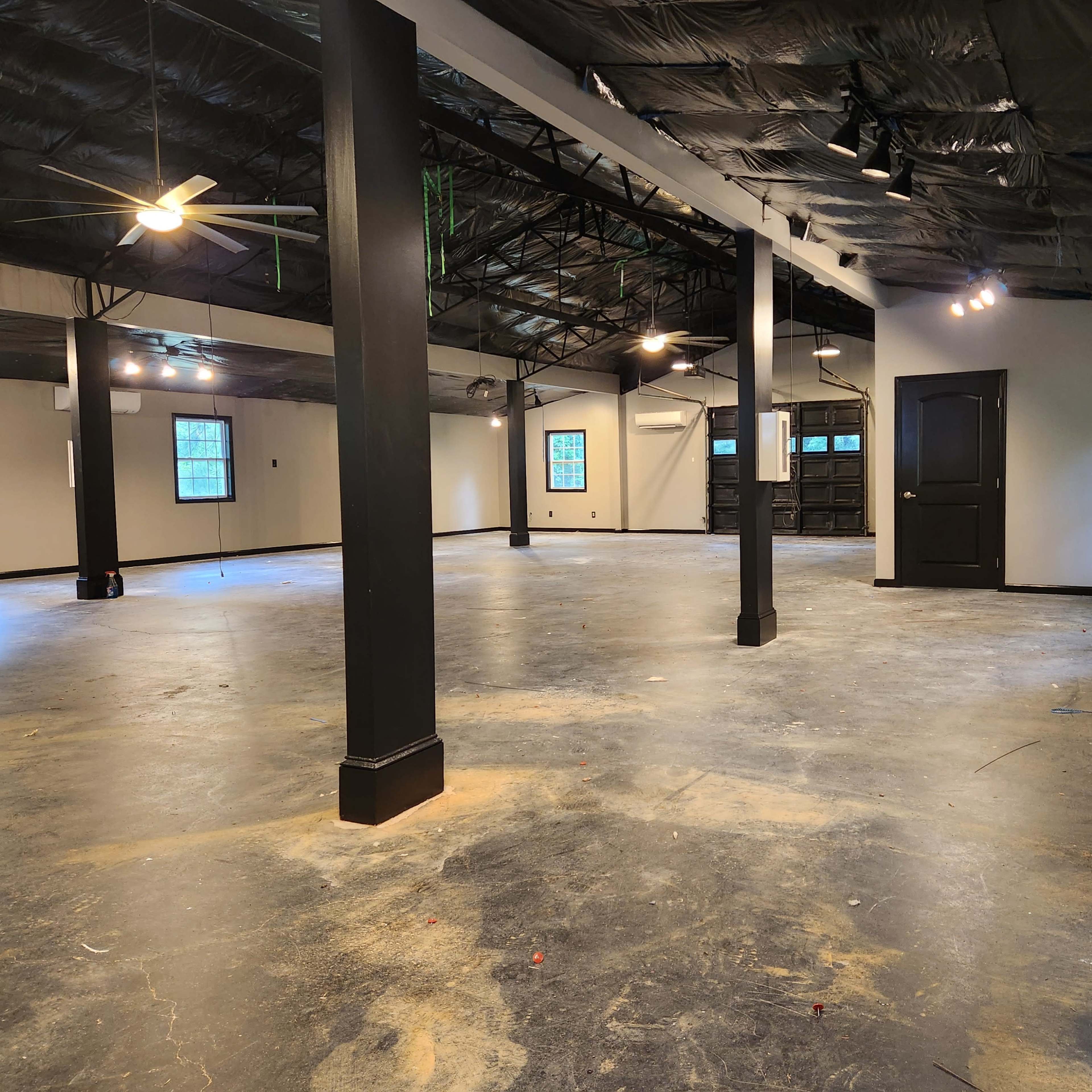 A large, empty room with a concrete floor, exposed beams, and multiple ceiling fans.