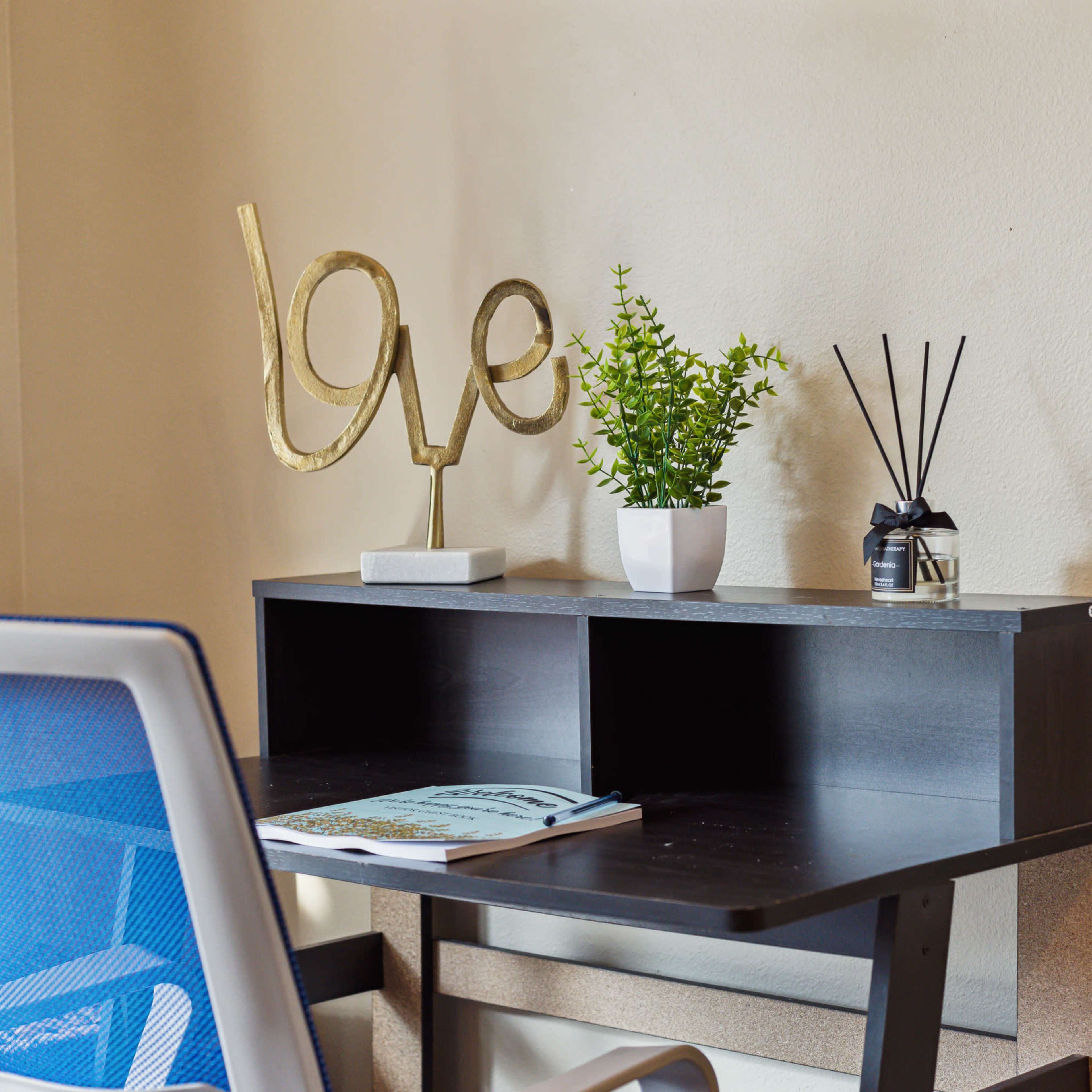 A modern desk with a blue office chair features a decorative gold sculpture, a small potted plant, and items arranged on the tabletop.
