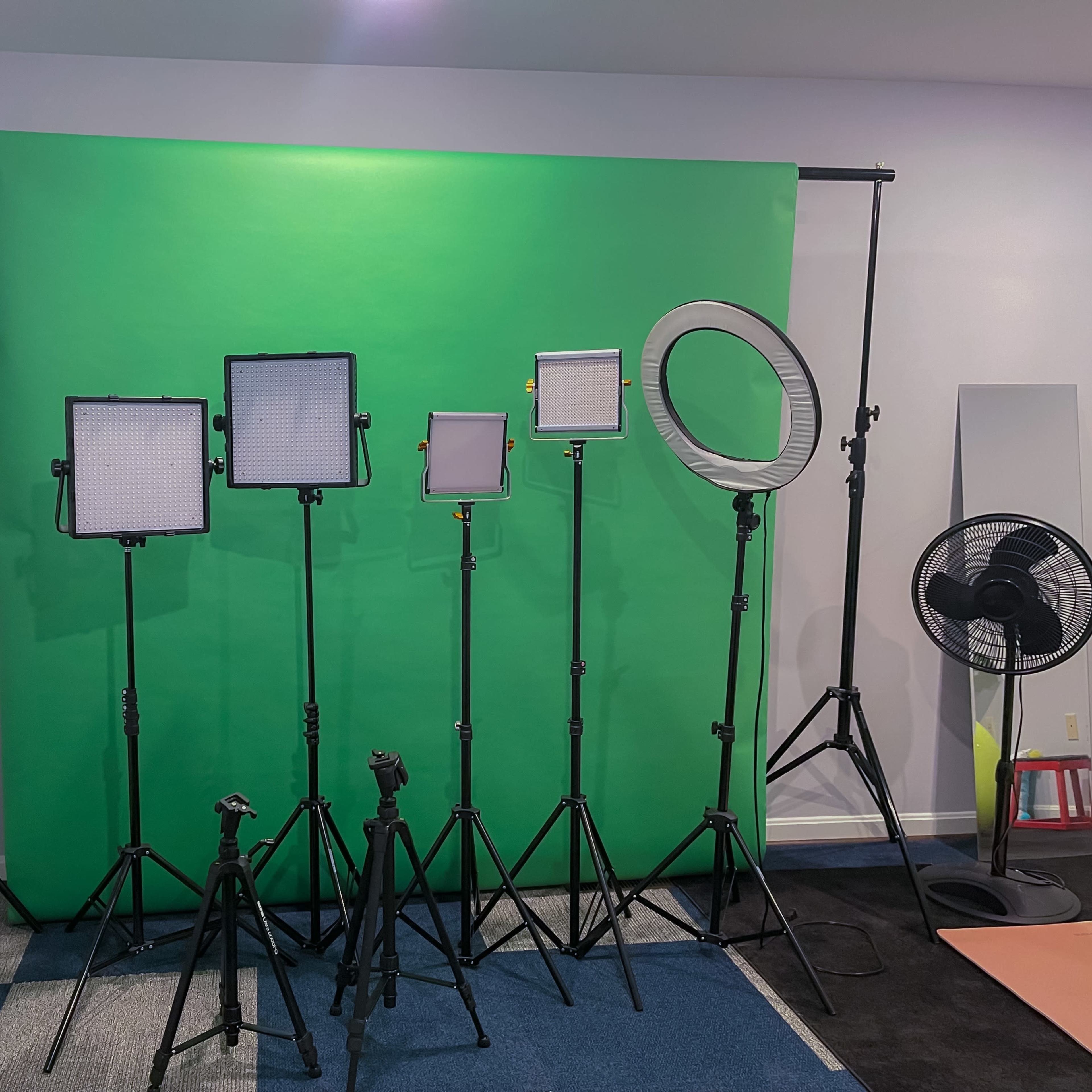 A green backdrop setup for video or photography, with multiple lighting fixtures positioned on stands.