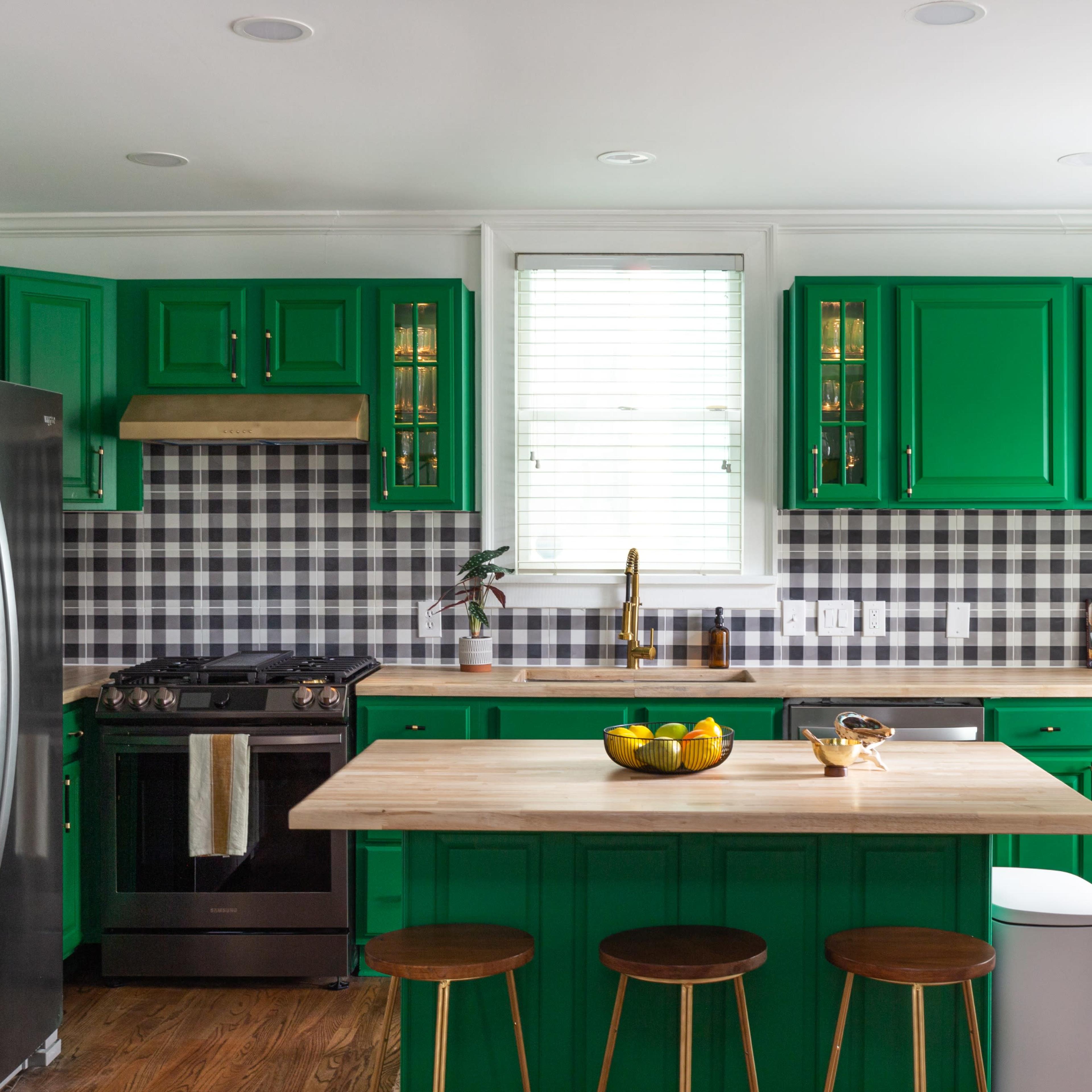 The kitchen features green cabinets, a stainless steel refrigerator, a checkered black and white backsplash, and a wooden island with three stools.