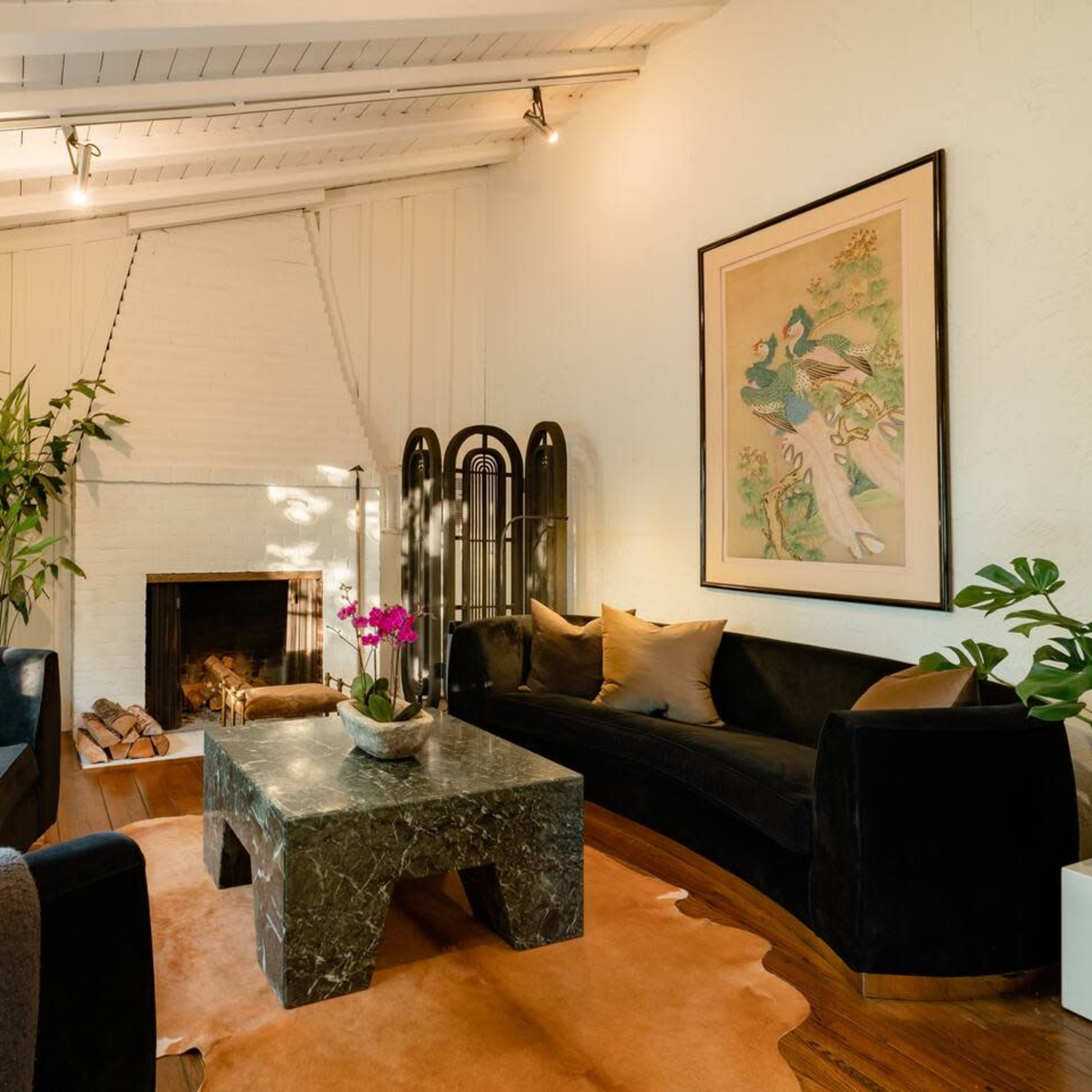 A stylish living room featuring a fireplace, a large green marble coffee table, and a mix of seating arrangements with plants and artwork on the walls.