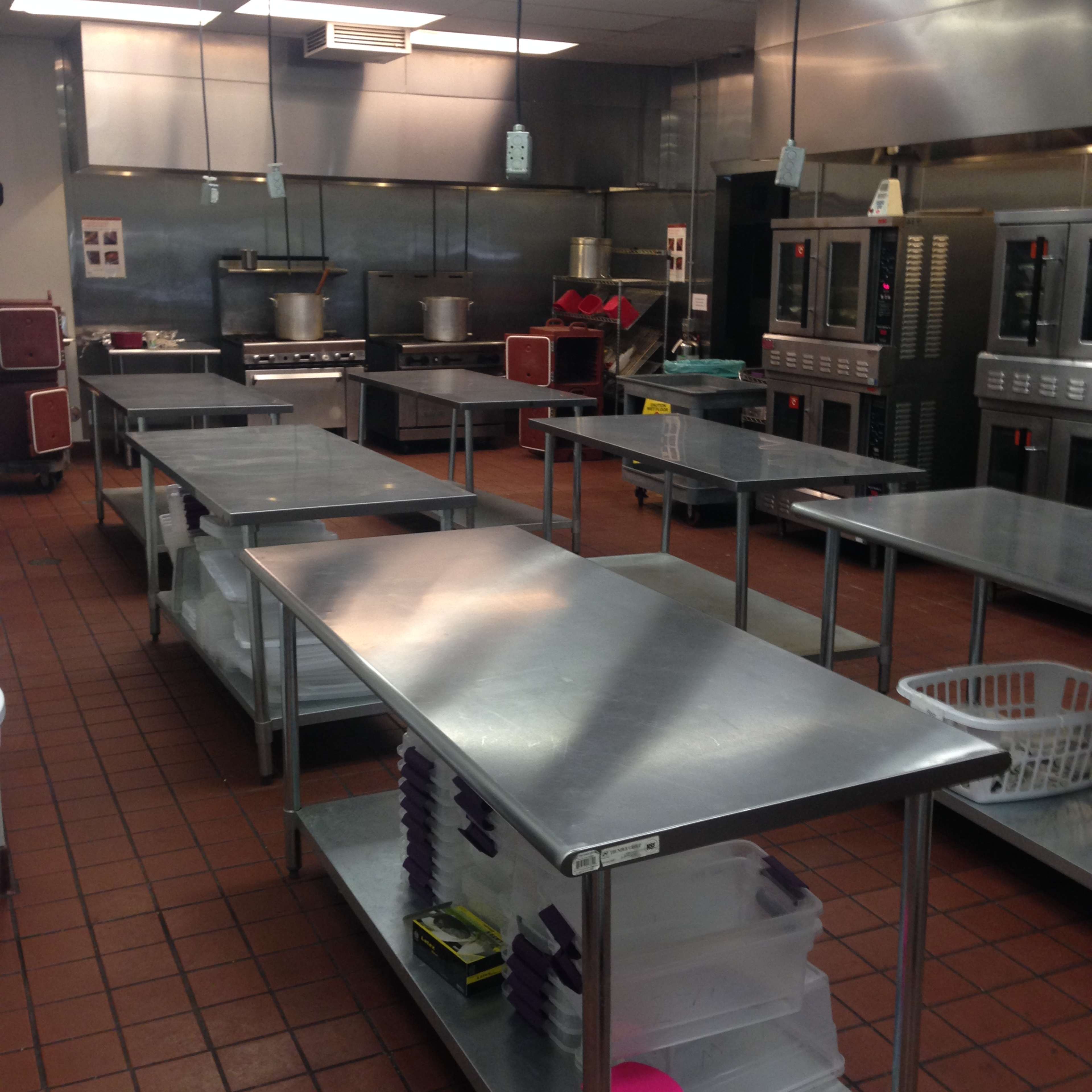 A spacious commercial kitchen with stainless steel tables, large cooking equipment, and an organized layout.