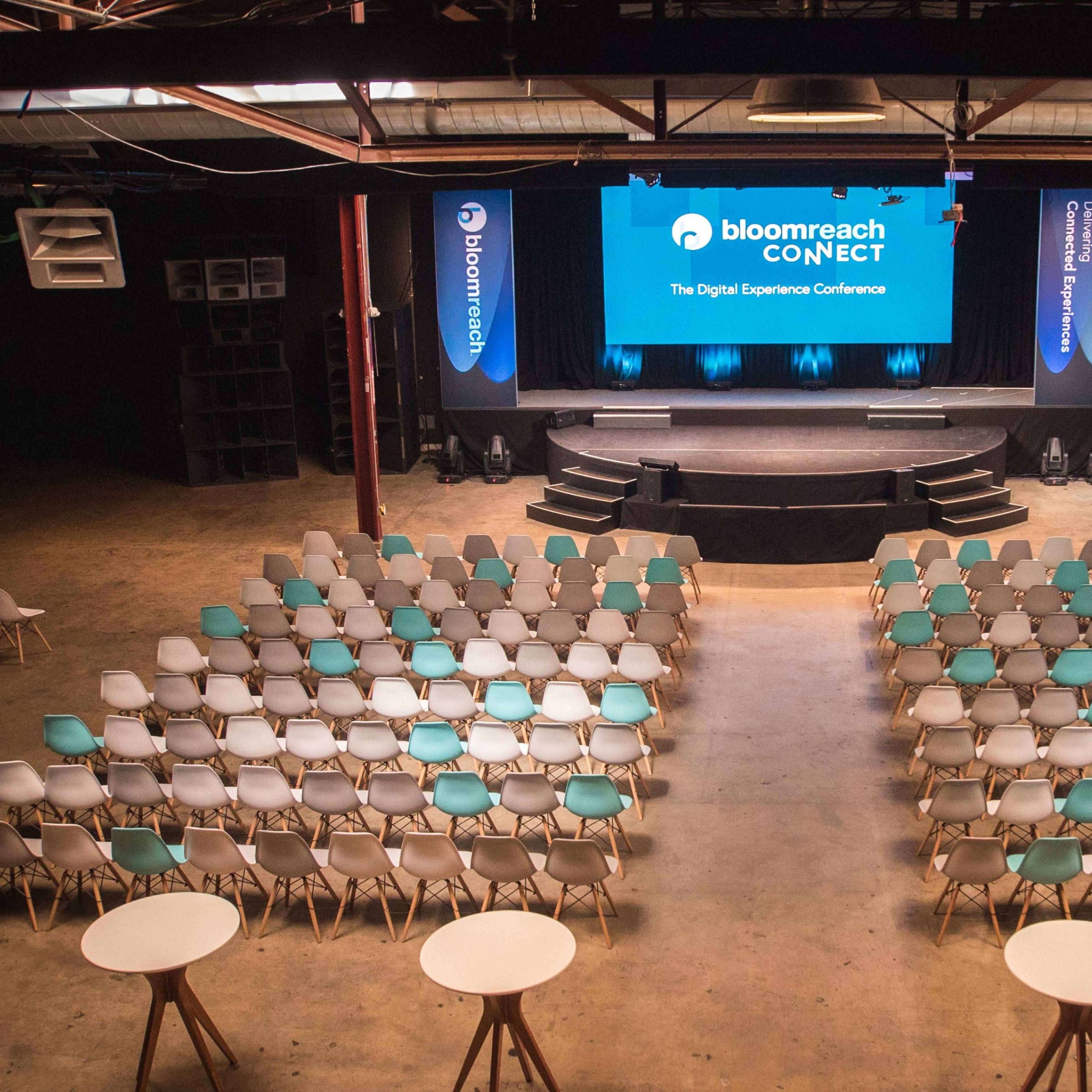 A spacious conference venue set up for the bloomreach CONNECT event, featuring rows of chairs facing a stage with a large screen.