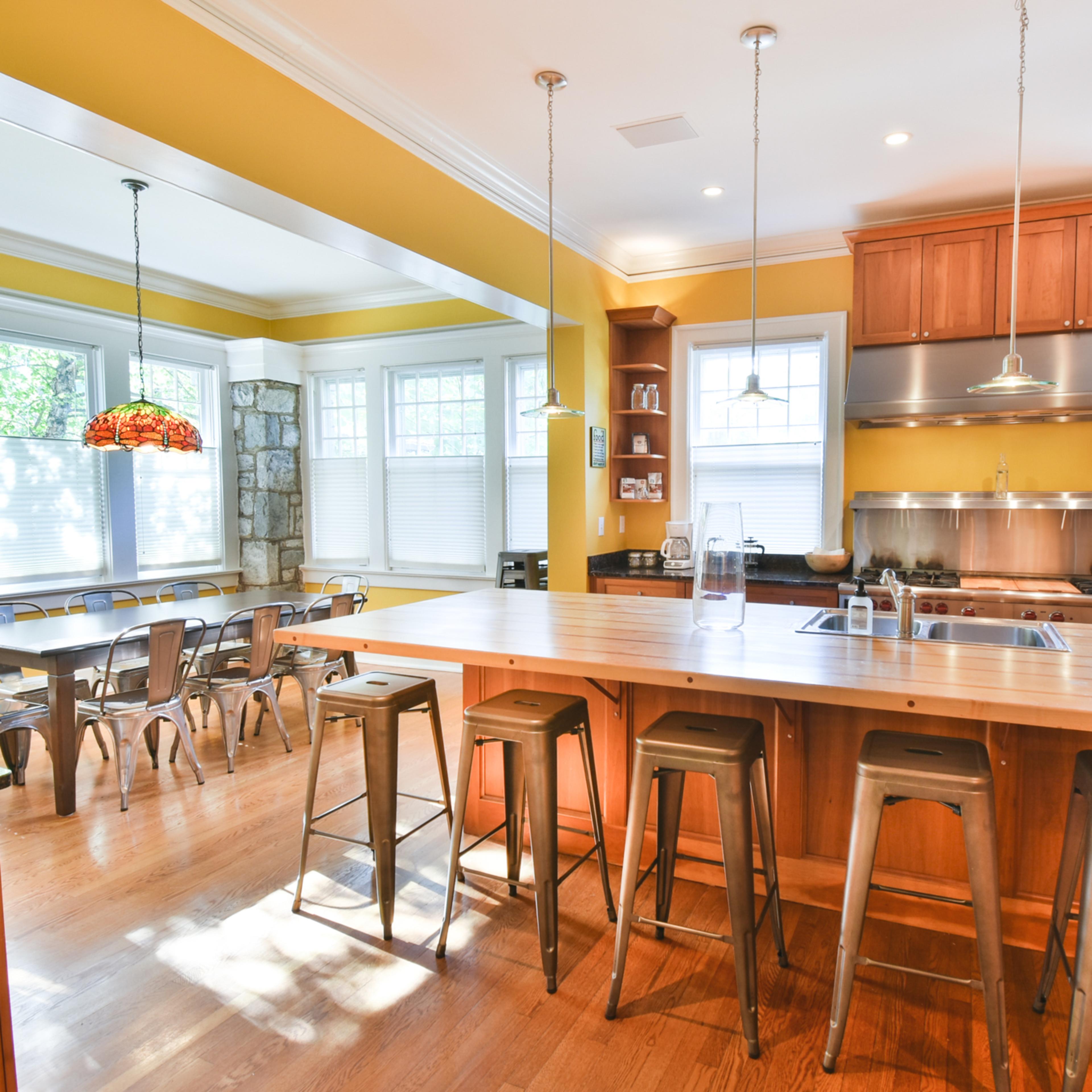 A spacious kitchen with wooden cabinets, a large island with bar stools, and a dining area featuring a set of tables and chairs.