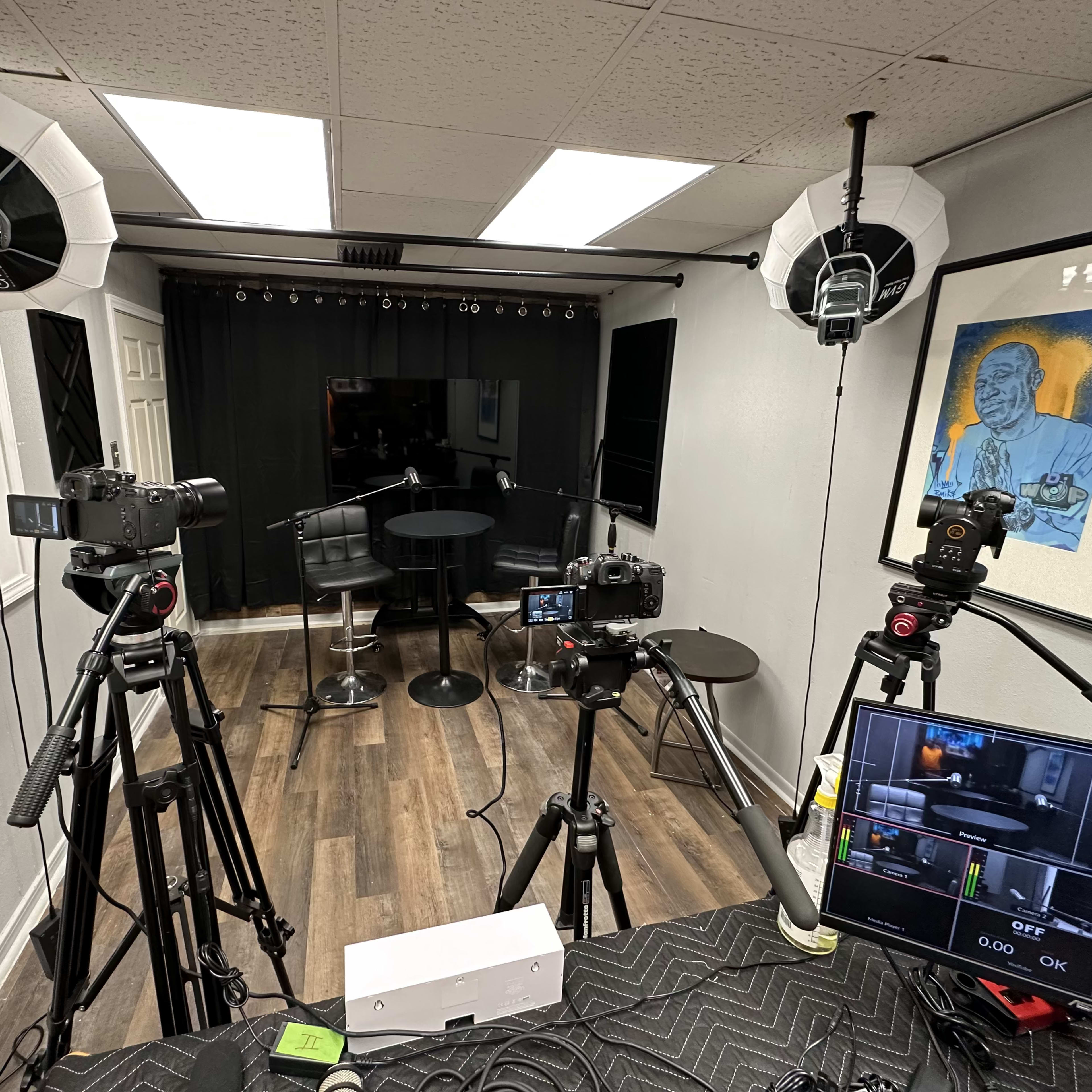 A filming setup with multiple cameras and lighting equipment arranged around a small black table in a studio space.