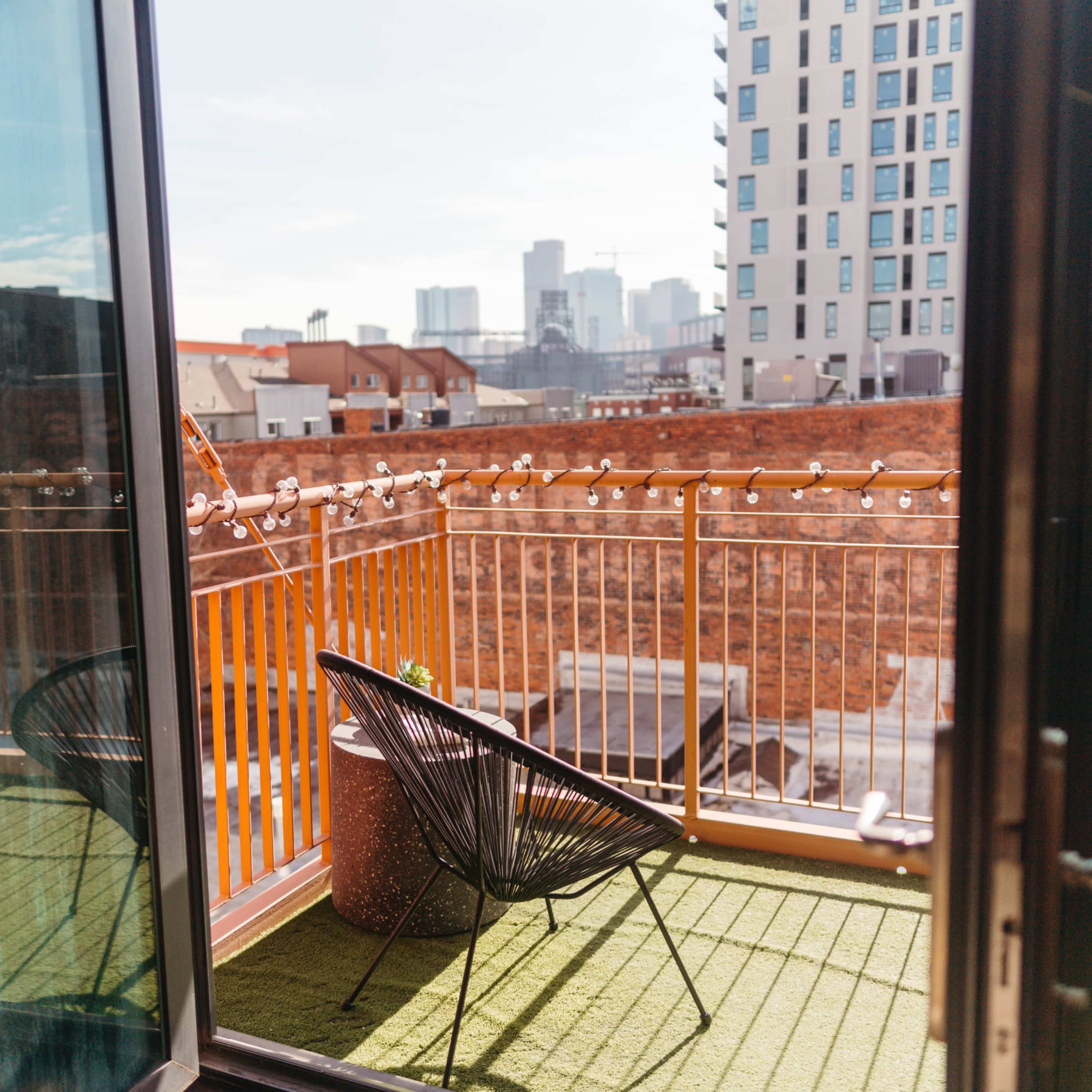 A balcony with two chairs, a small table, and a view of a city skyline in the background.