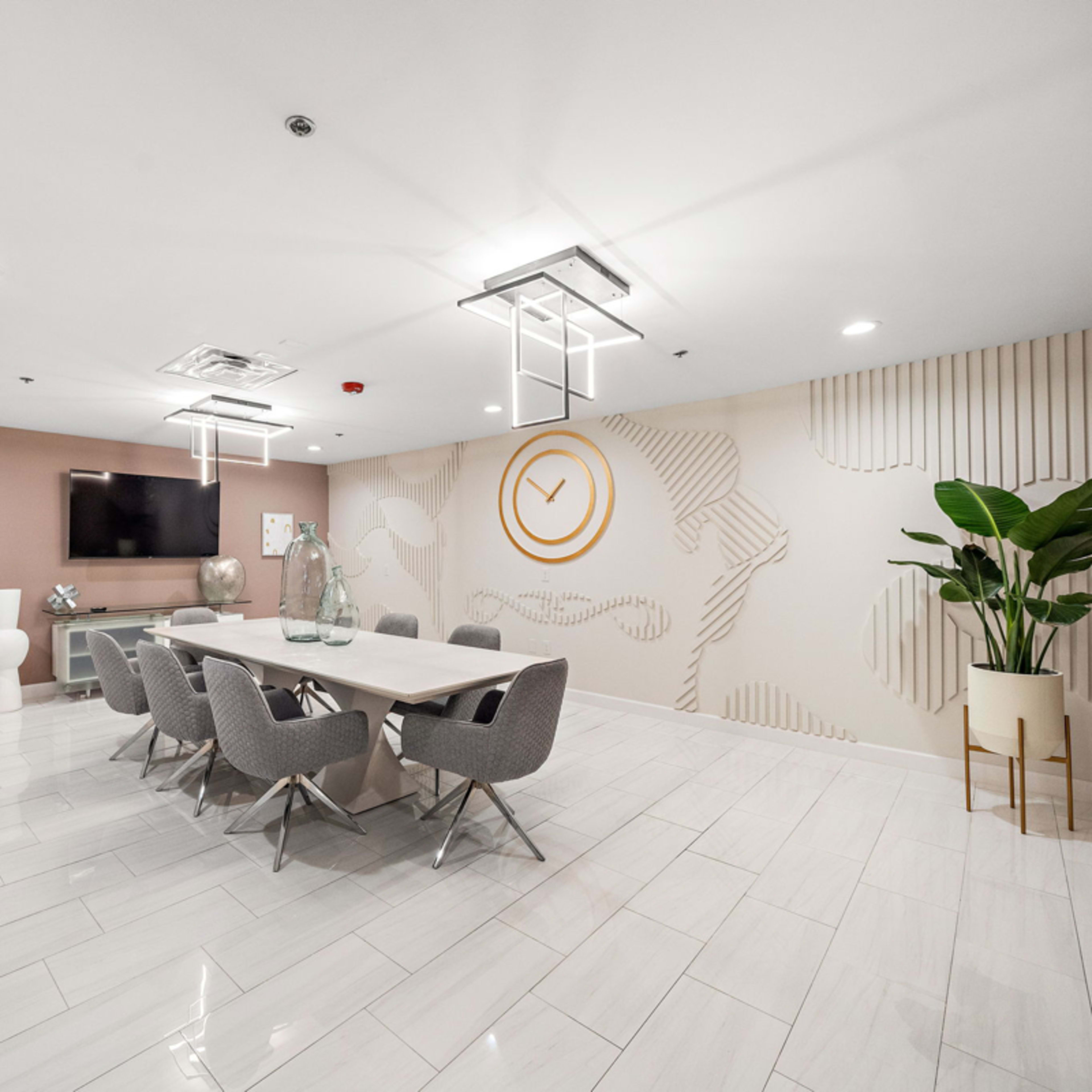 A modern lounge area with blue velvet seating, gold accents, and a colorful accent wall featuring floral designs, leading to a kitchen space in the background.