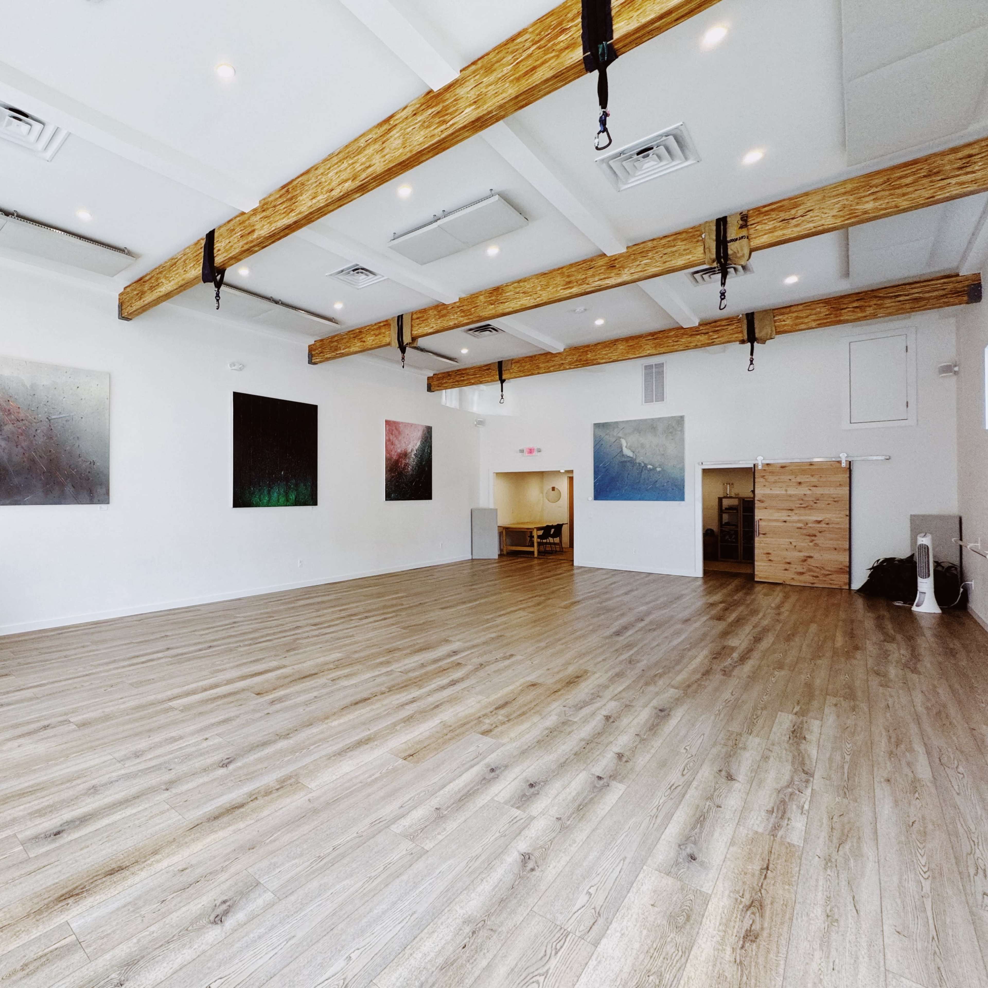 A spacious, well-lit room with wooden beams and large abstract paintings on the walls.