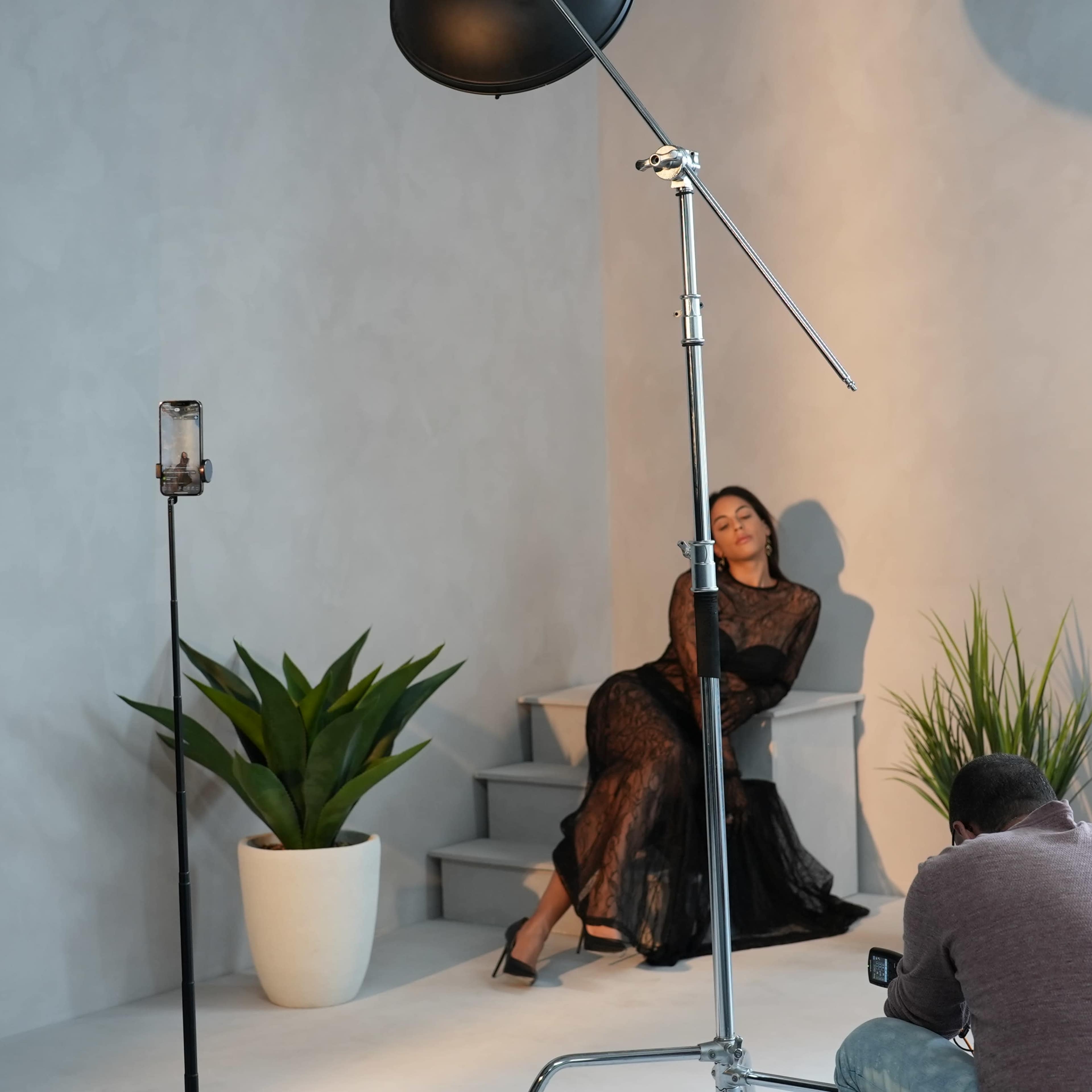 A model poses on steps in a minimalist photo studio while a photographer captures the shot.