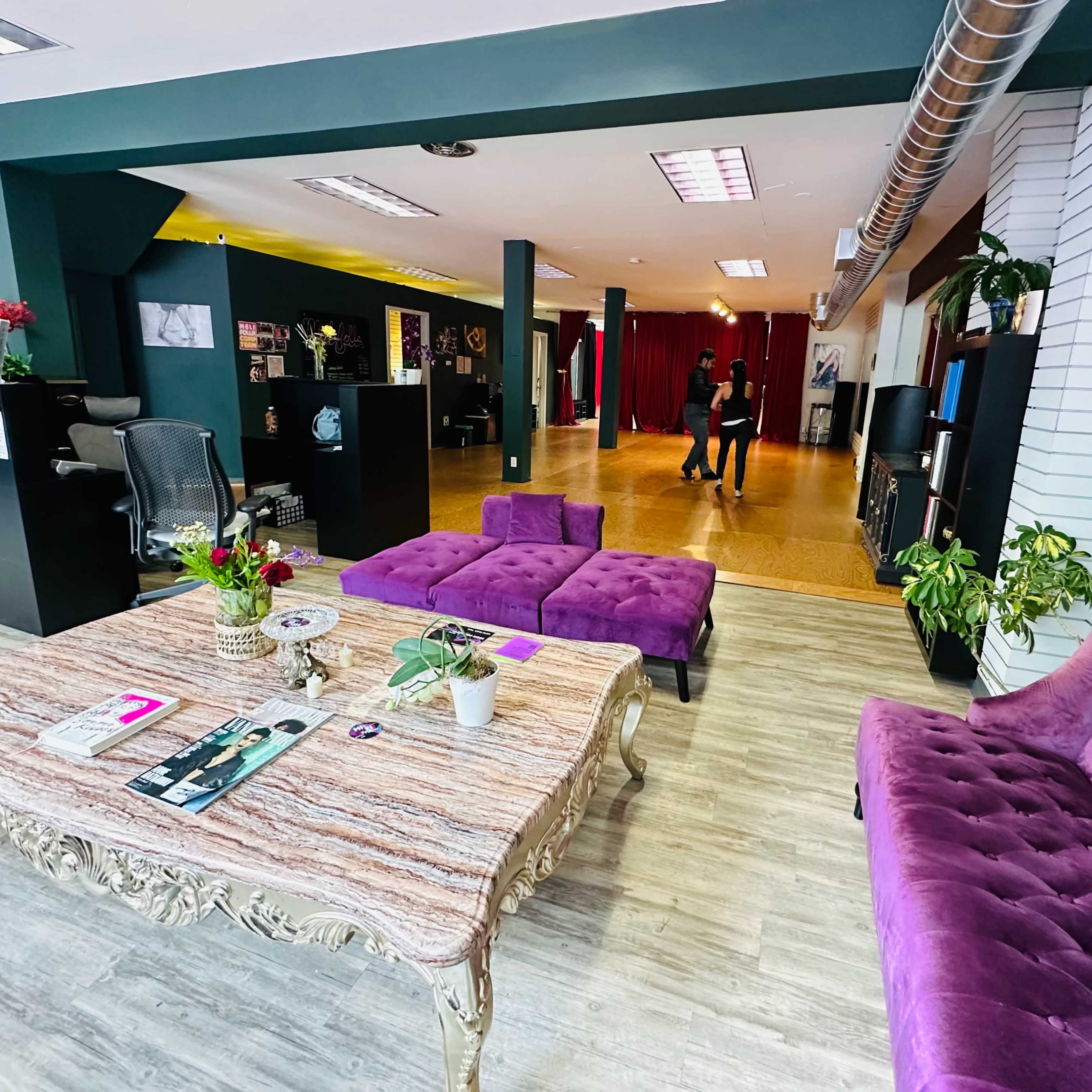 A lounge area with purple furniture, a decorative table, and an open space in the background where two people are interacting.