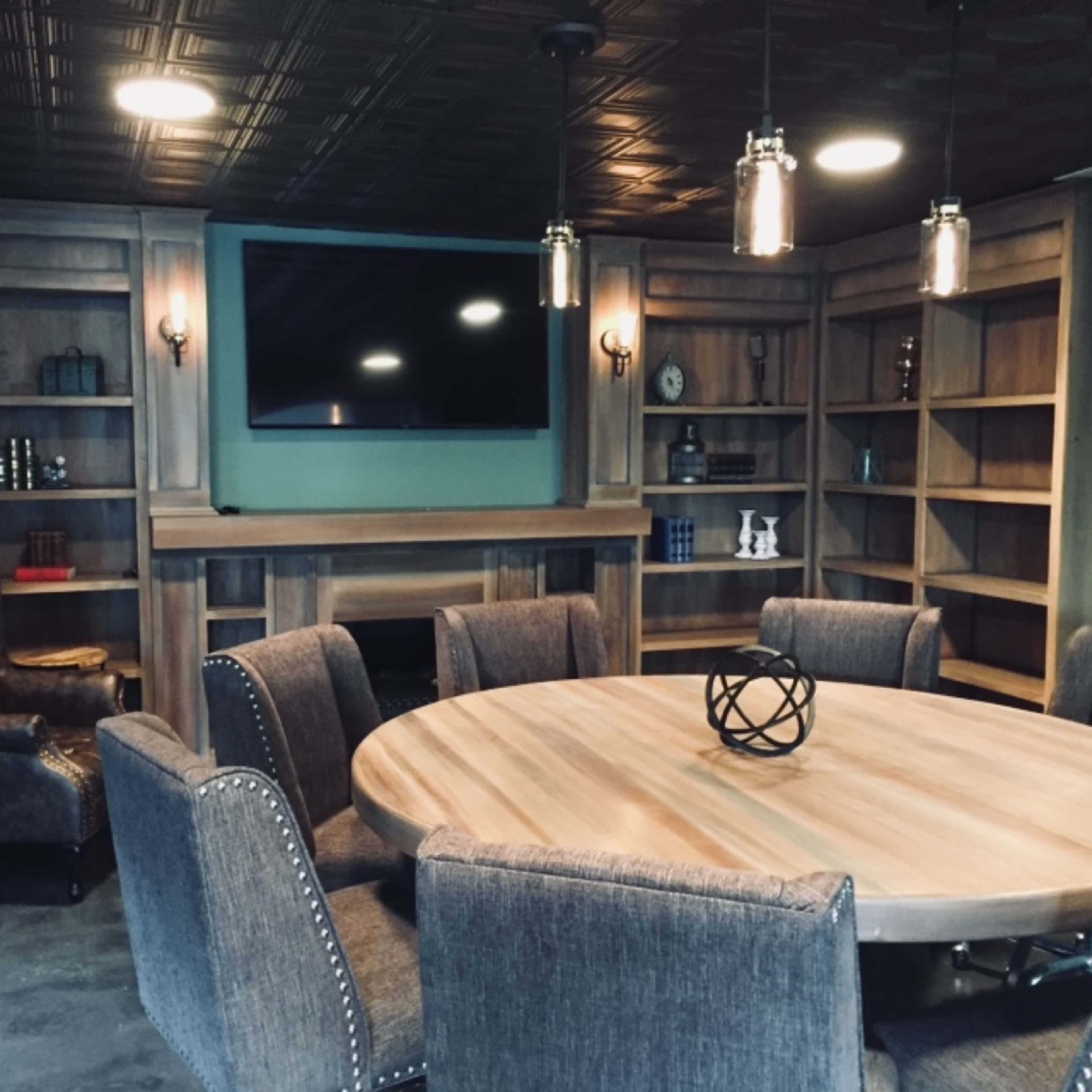 A cozy room featuring a round wooden table surrounded by upholstered chairs, with built-in wooden shelves and a television mounted on the wall.