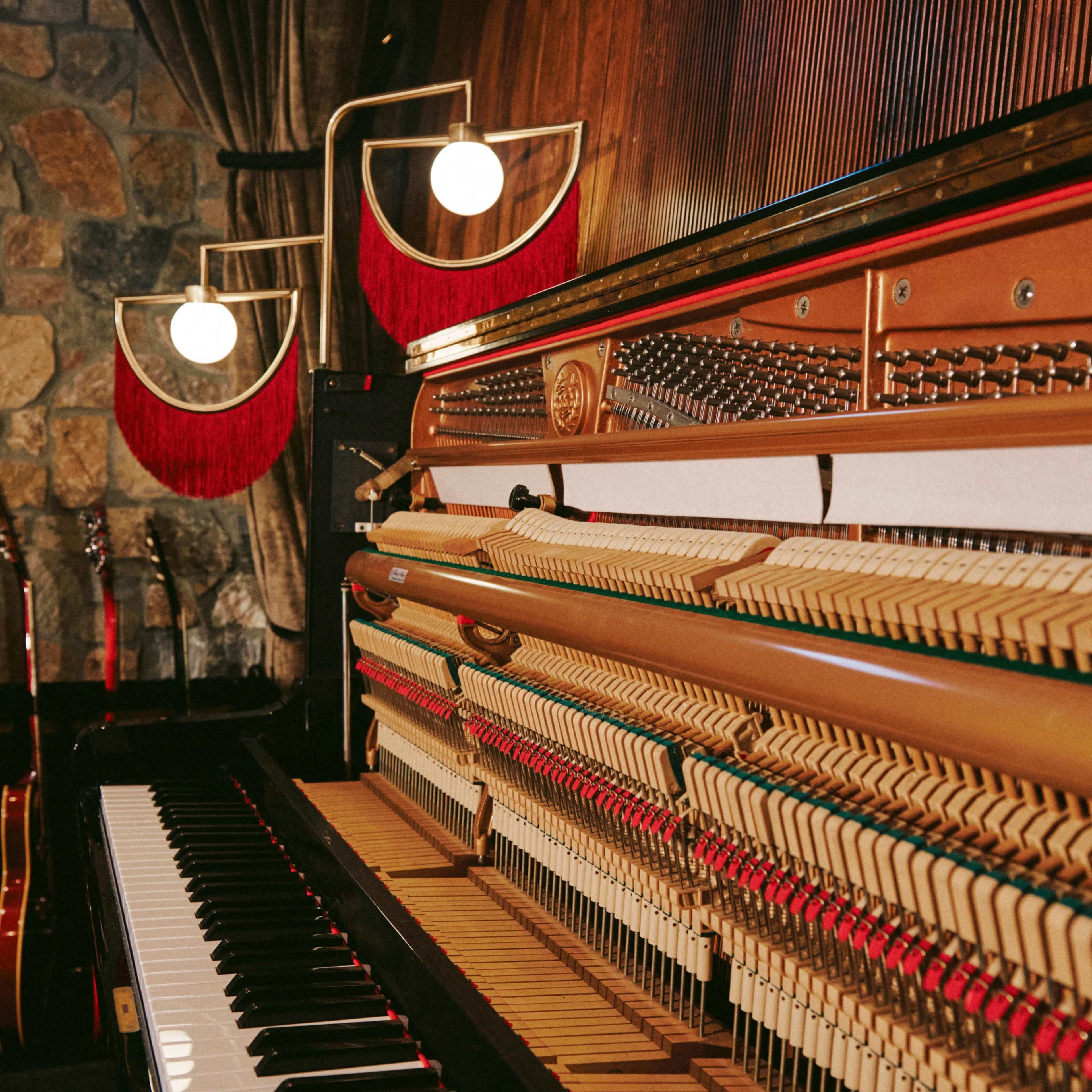 A close-up view of the interior mechanism of a grand piano with a wooden wall and decorative lighting in the background.