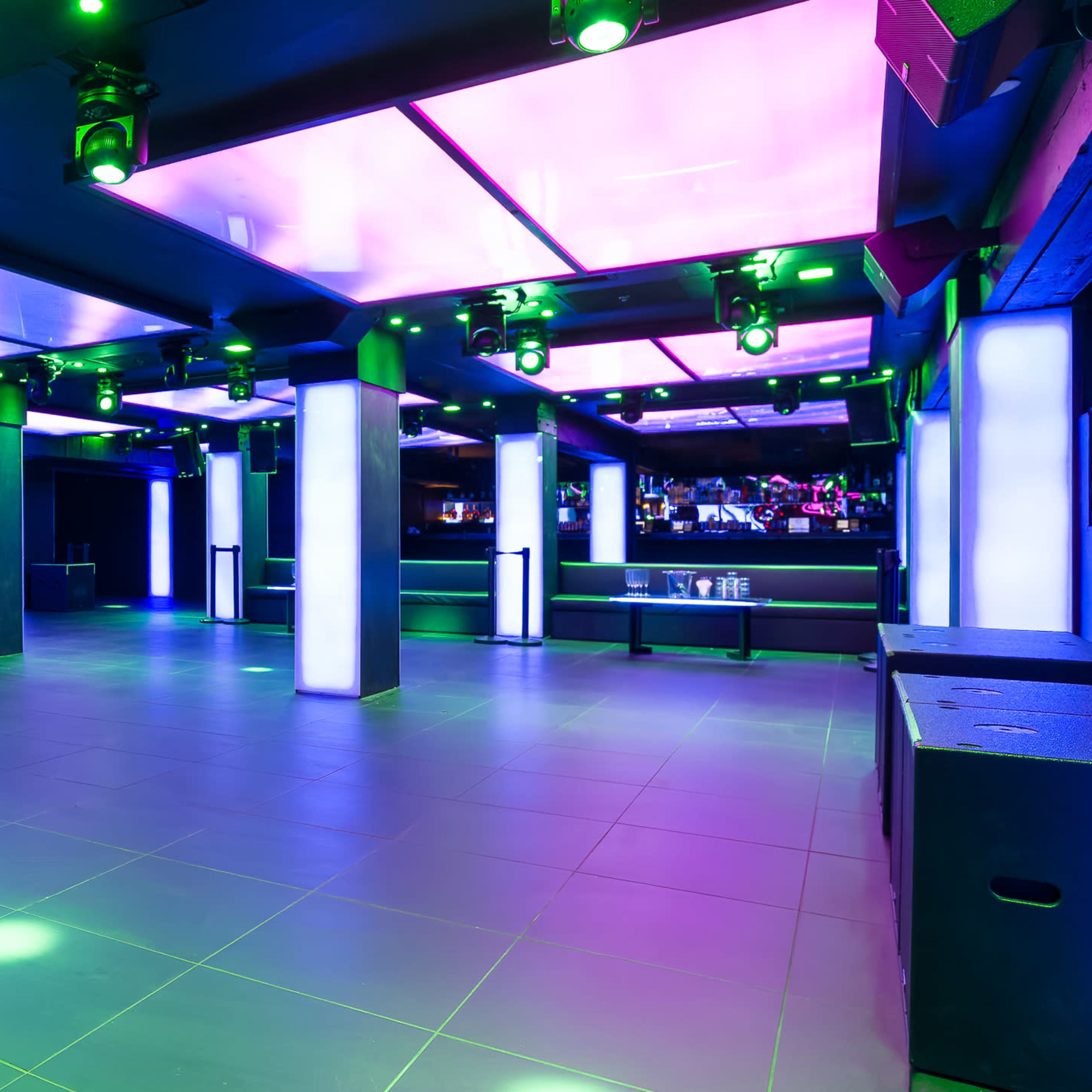 A spacious nightclub interior with illuminated columns and colored lighting fixtures on the ceiling.
