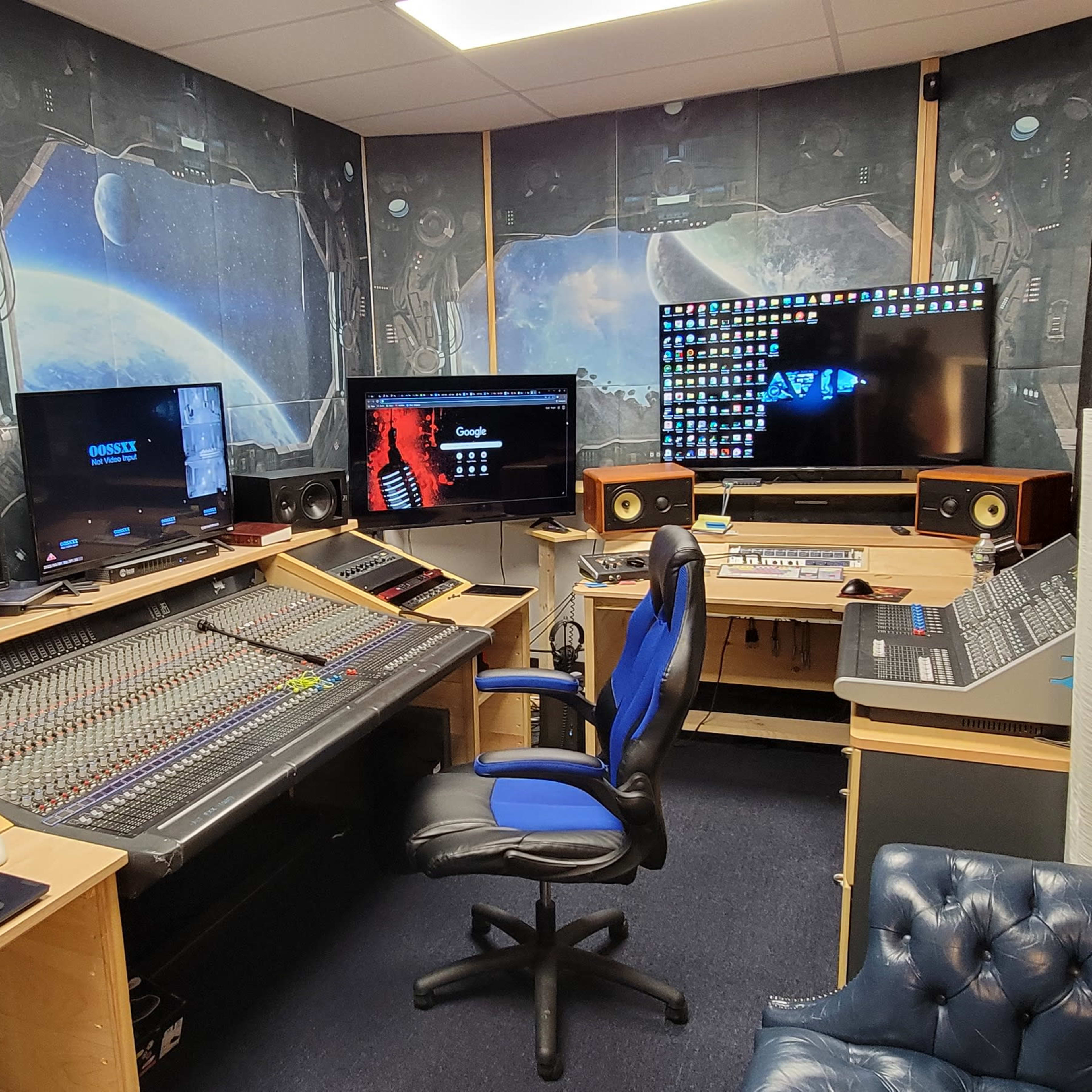 A recording studio featuring a large mixing console, computer monitors, and a blue office chair, all set against a space-themed backdrop.