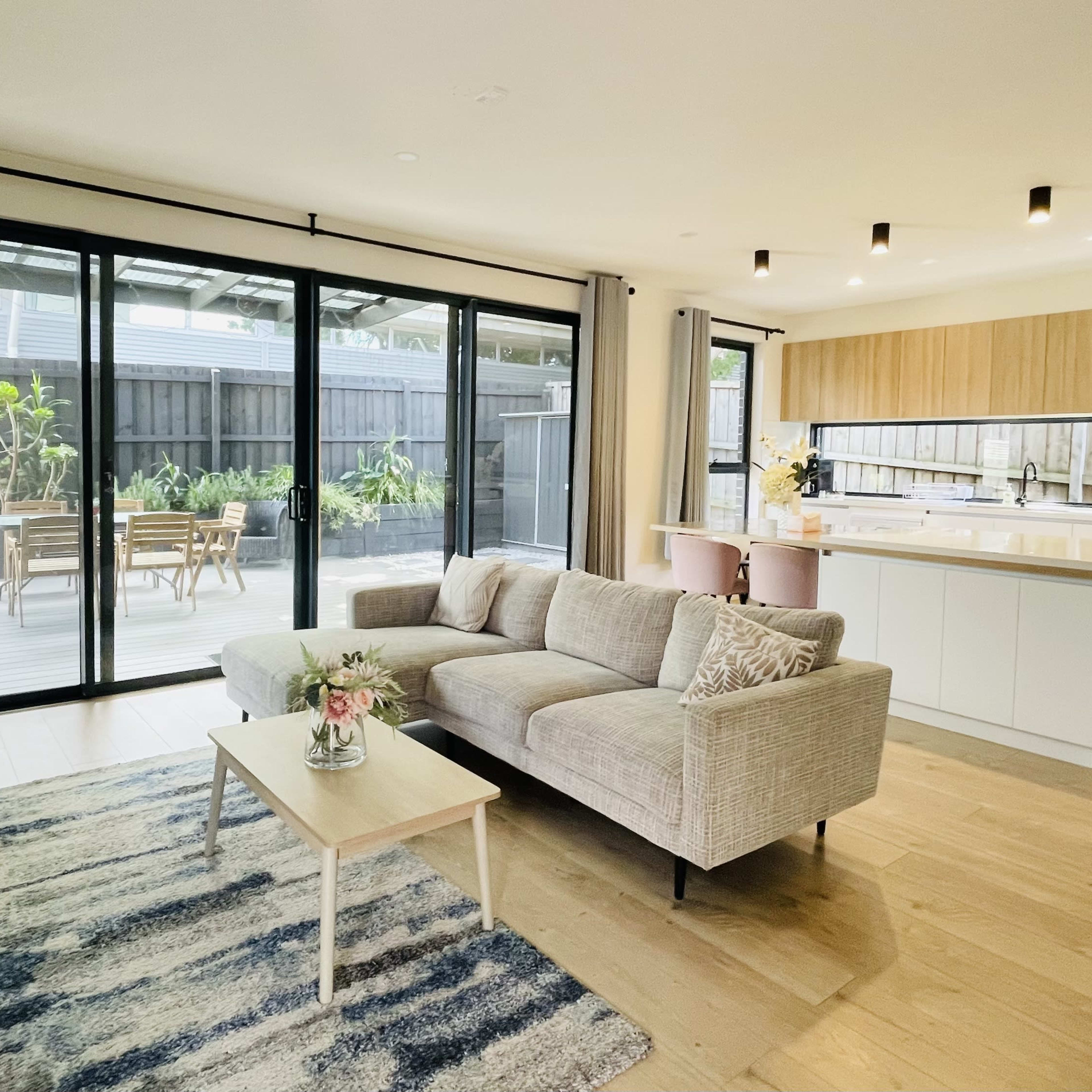 A modern living room with a light-colored sofa, coffee table, and a large sliding glass door leading to an outdoor deck area with patio furniture.