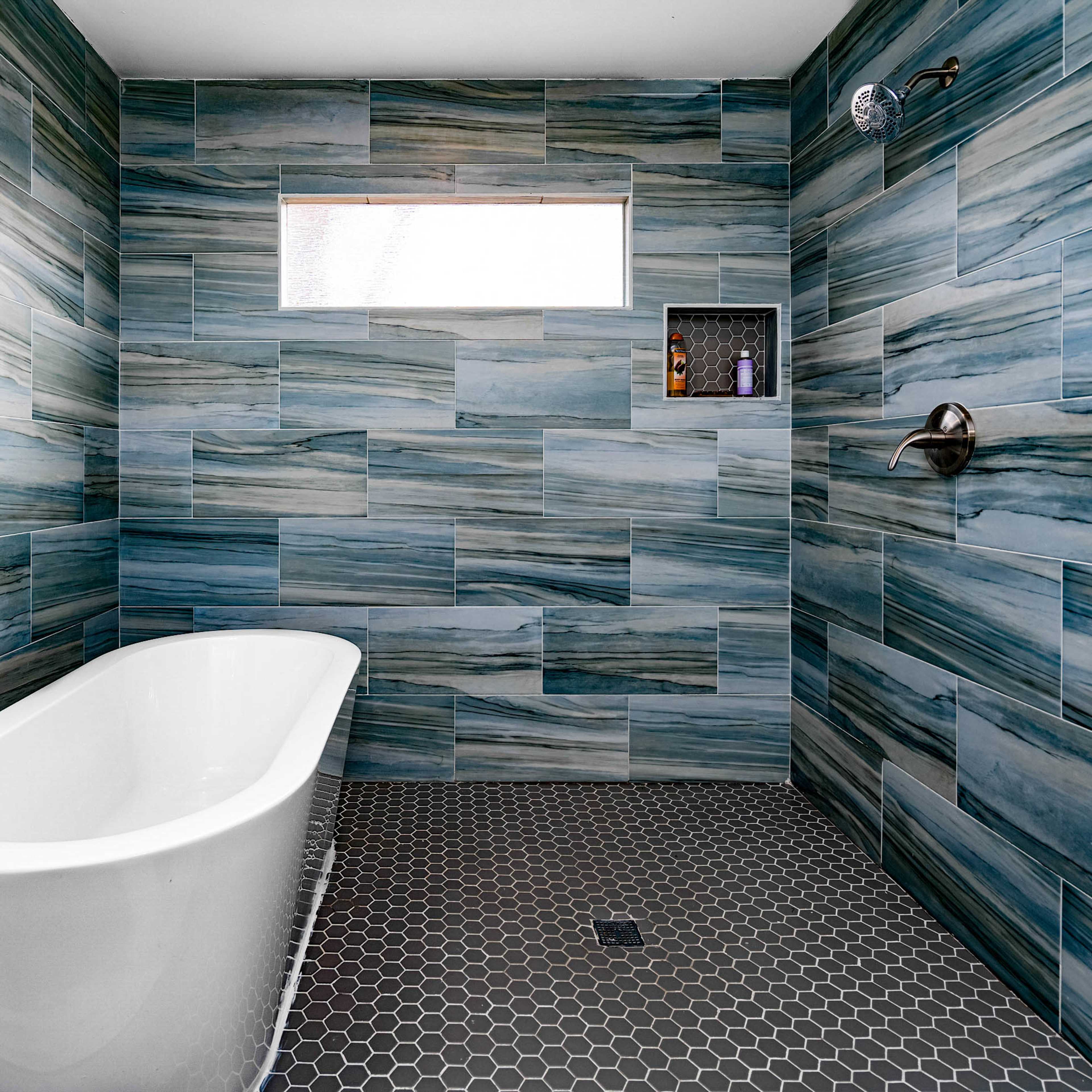 A modern bathroom with blue patterned wall tiles, a freestanding white bathtub, and a black hexagonal tiled floor.
