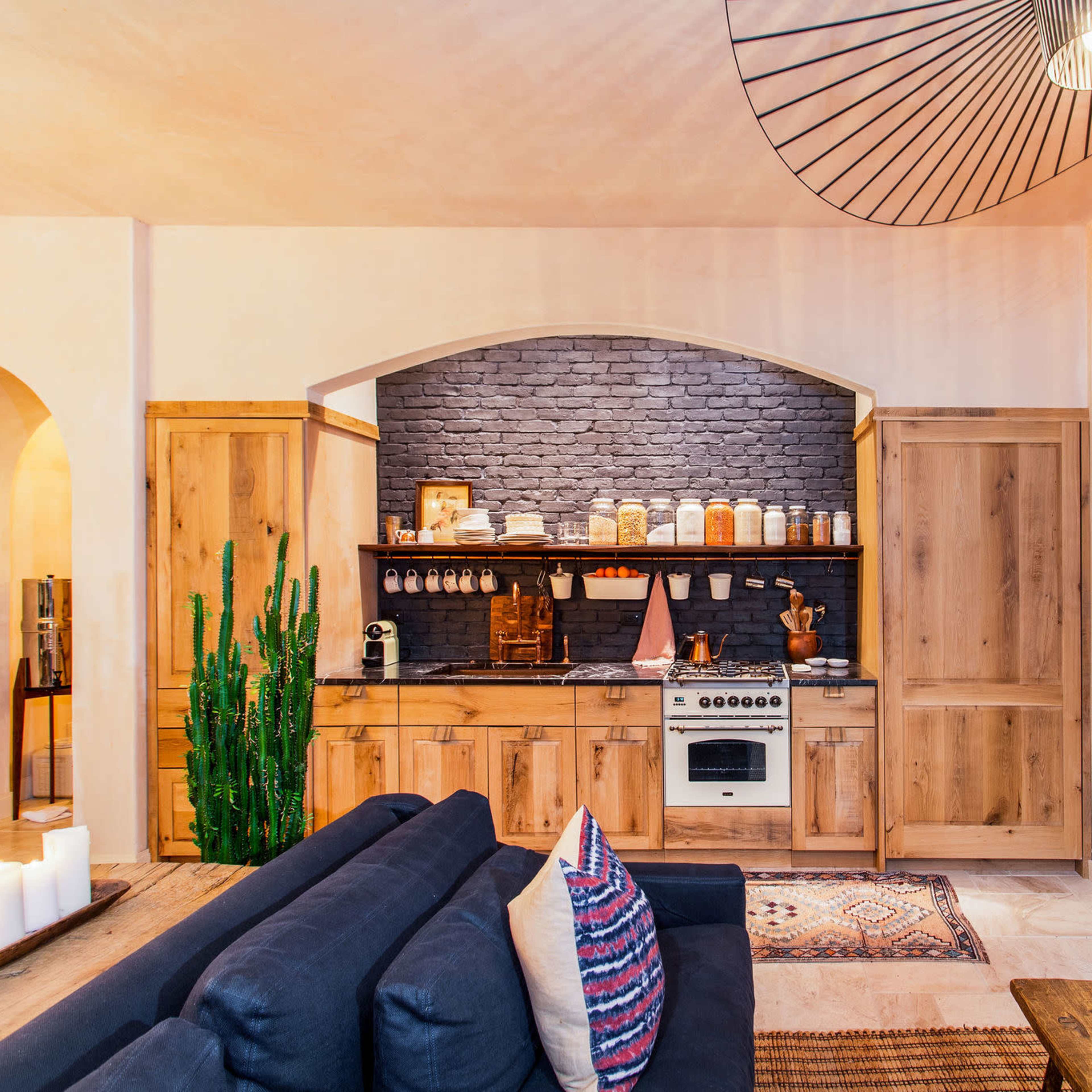 A modern kitchen features wooden cabinetry, a stone backsplash, and a gas stove, with a cozy living area visible in the foreground.