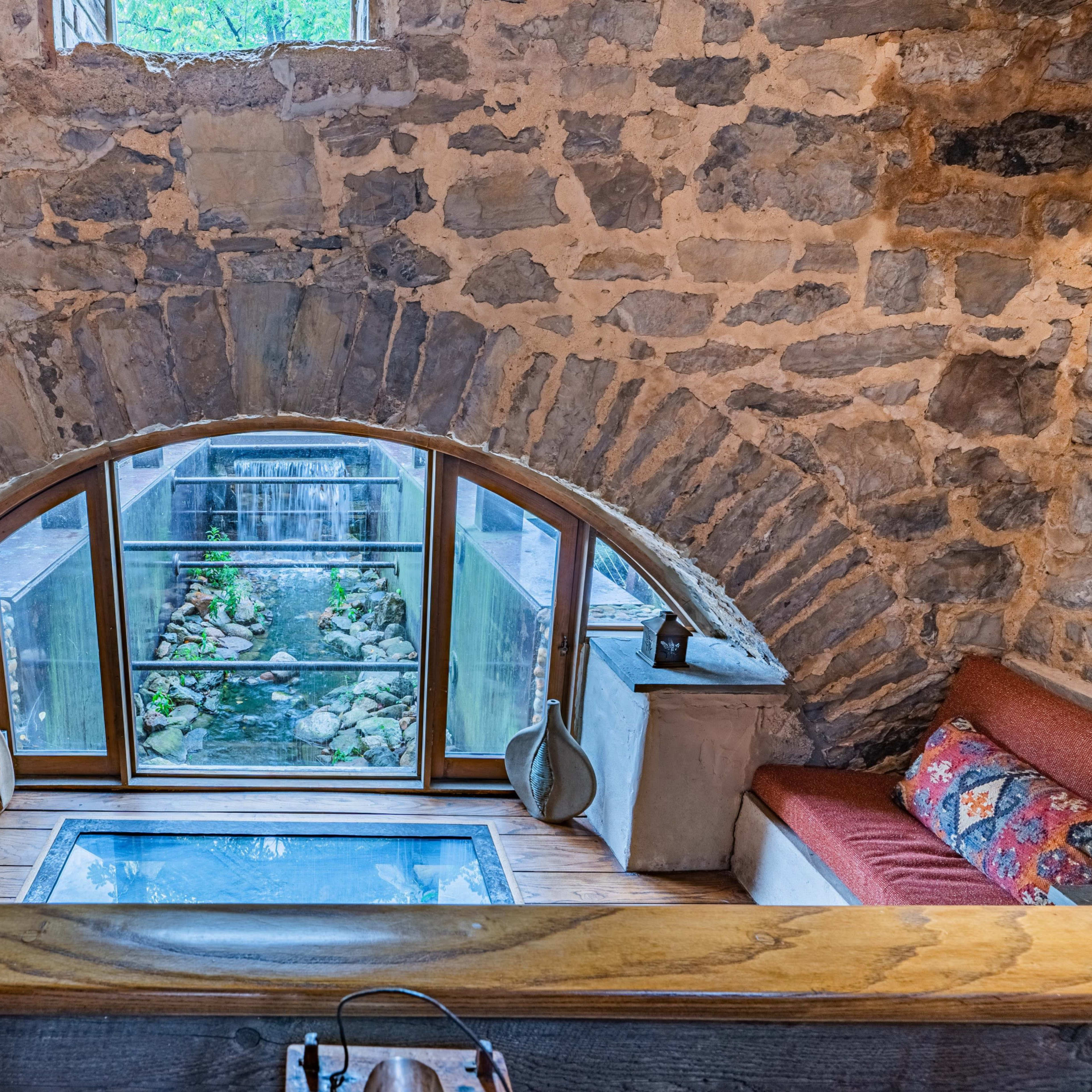 A cozy interior featuring an arched stone window framing a view of a small water feature surrounded by greenery.