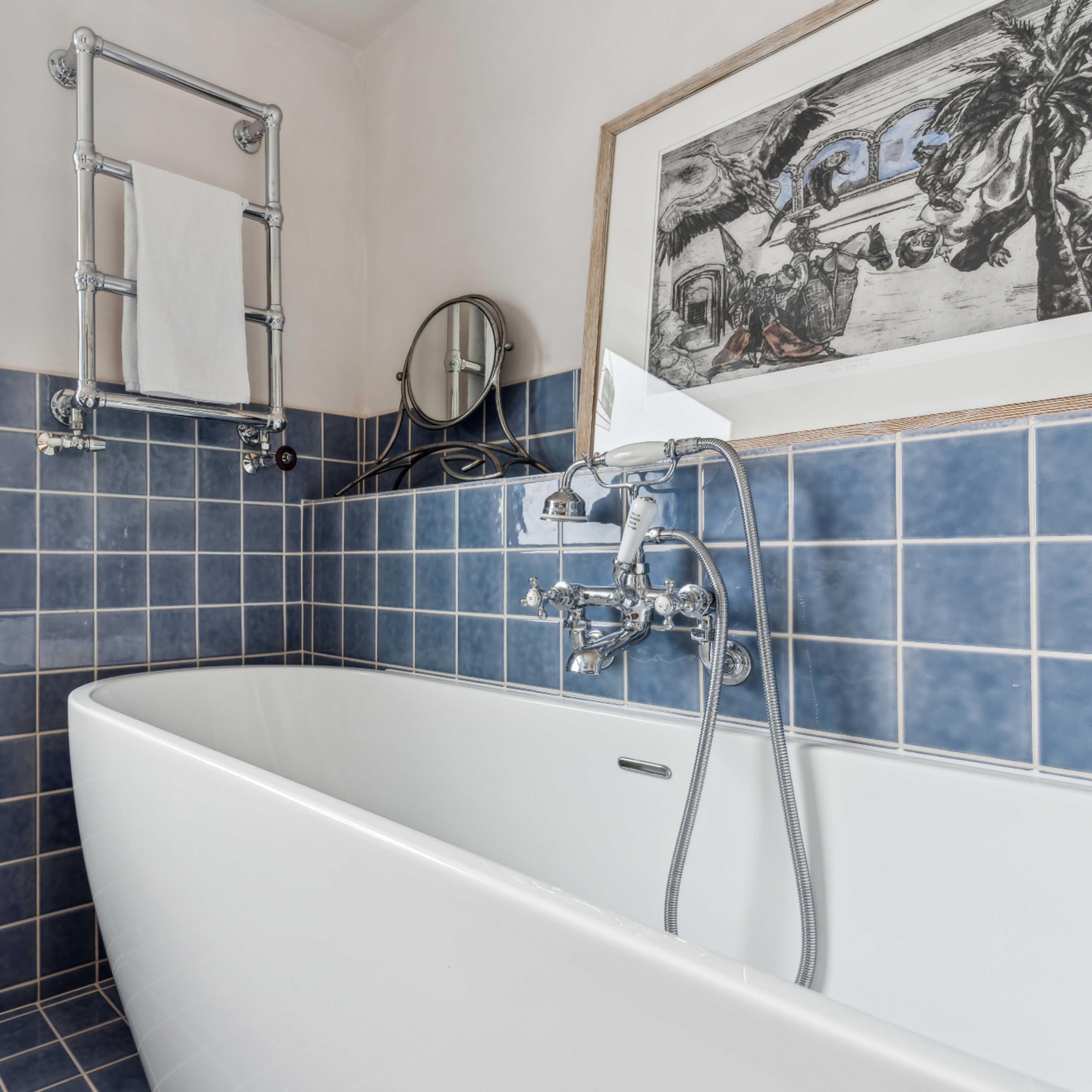 A bathroom featuring a white freestanding bathtub, blue tiled walls, and a wall-mounted mirror.