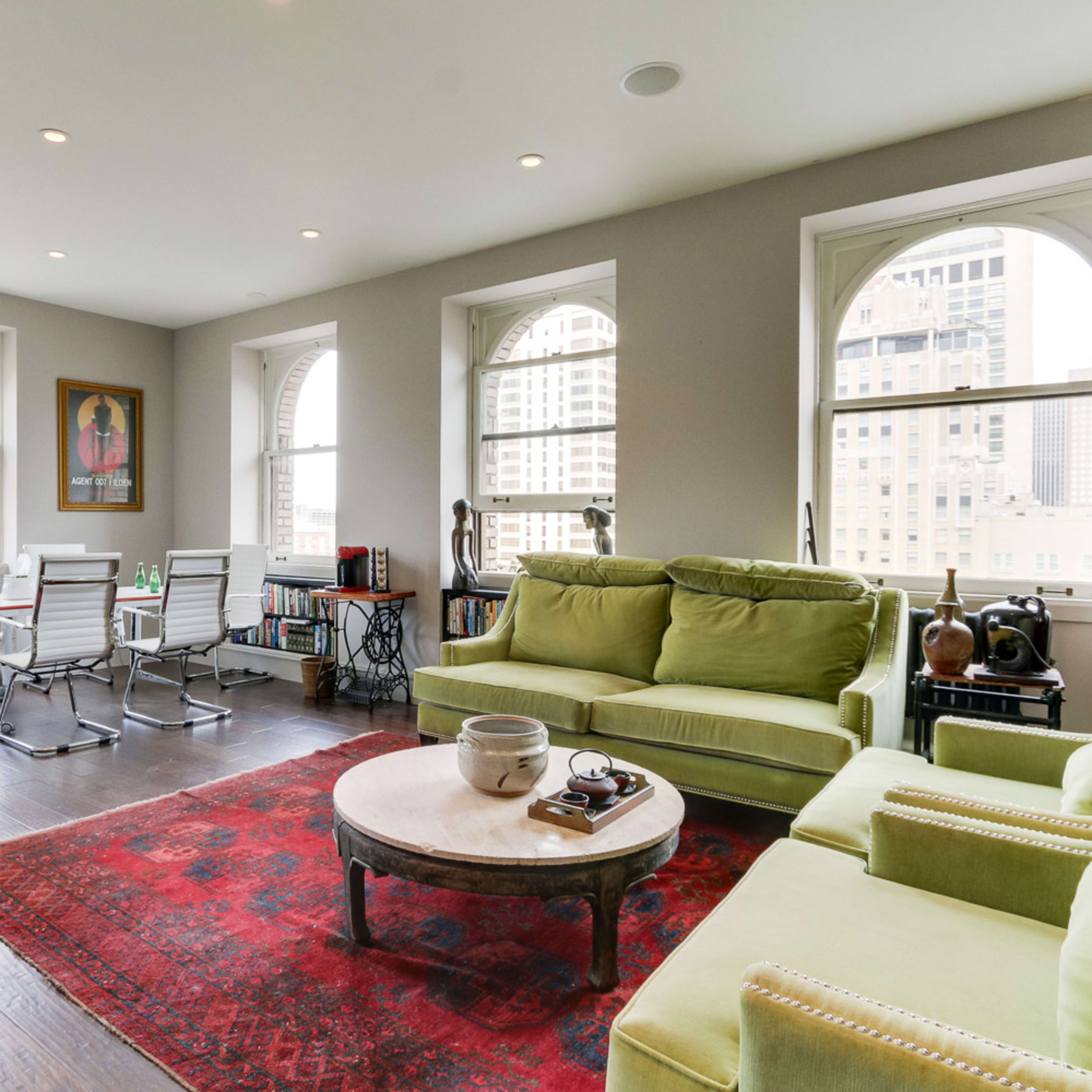 A modern living space featuring a green sofa, a round coffee table, and a dining area with several chairs near large windows.