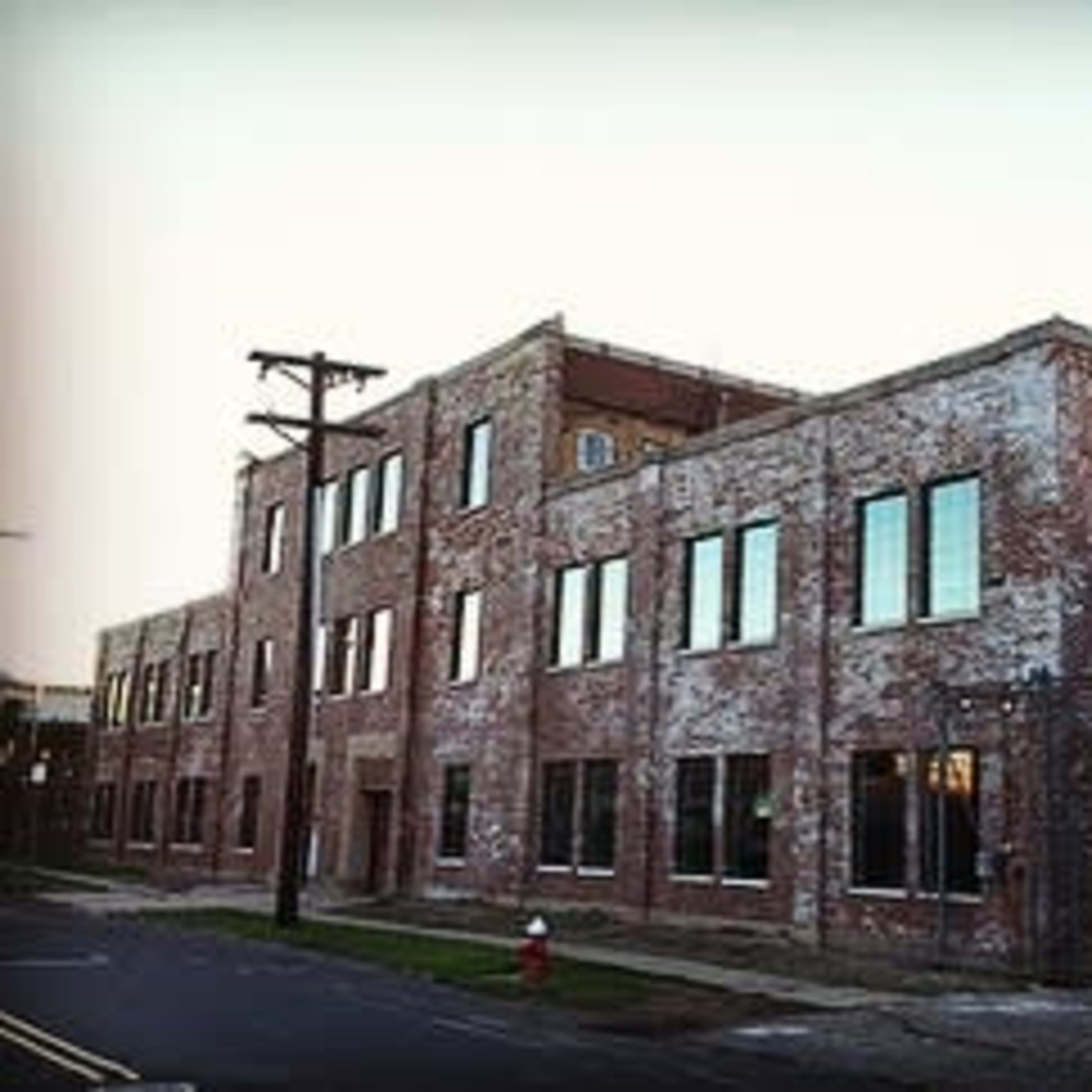 A large, brick building with multiple windows, located on a street with a fire hydrant nearby.