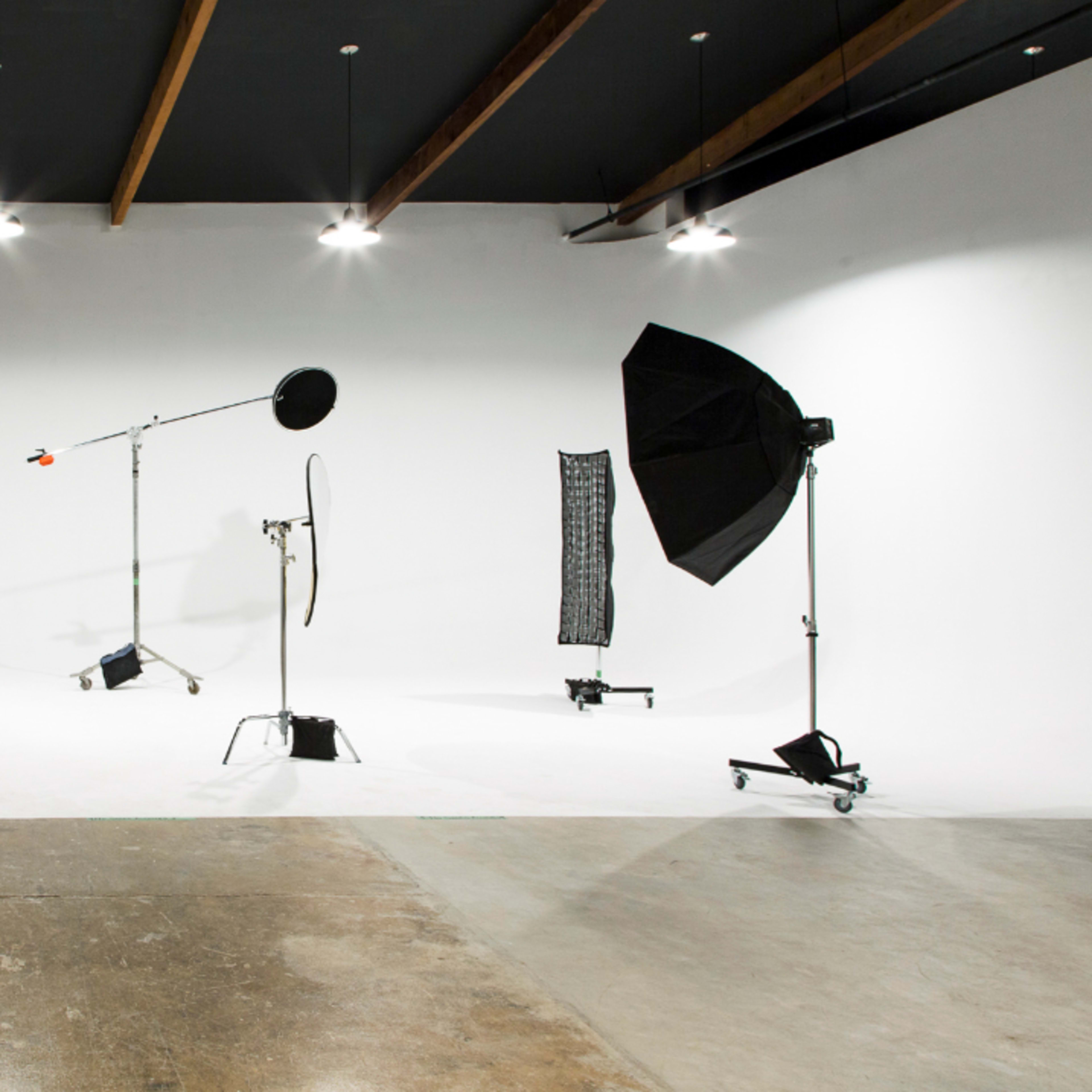A photography studio with a white backdrop and various lighting equipment, including a softbox and a light stand.