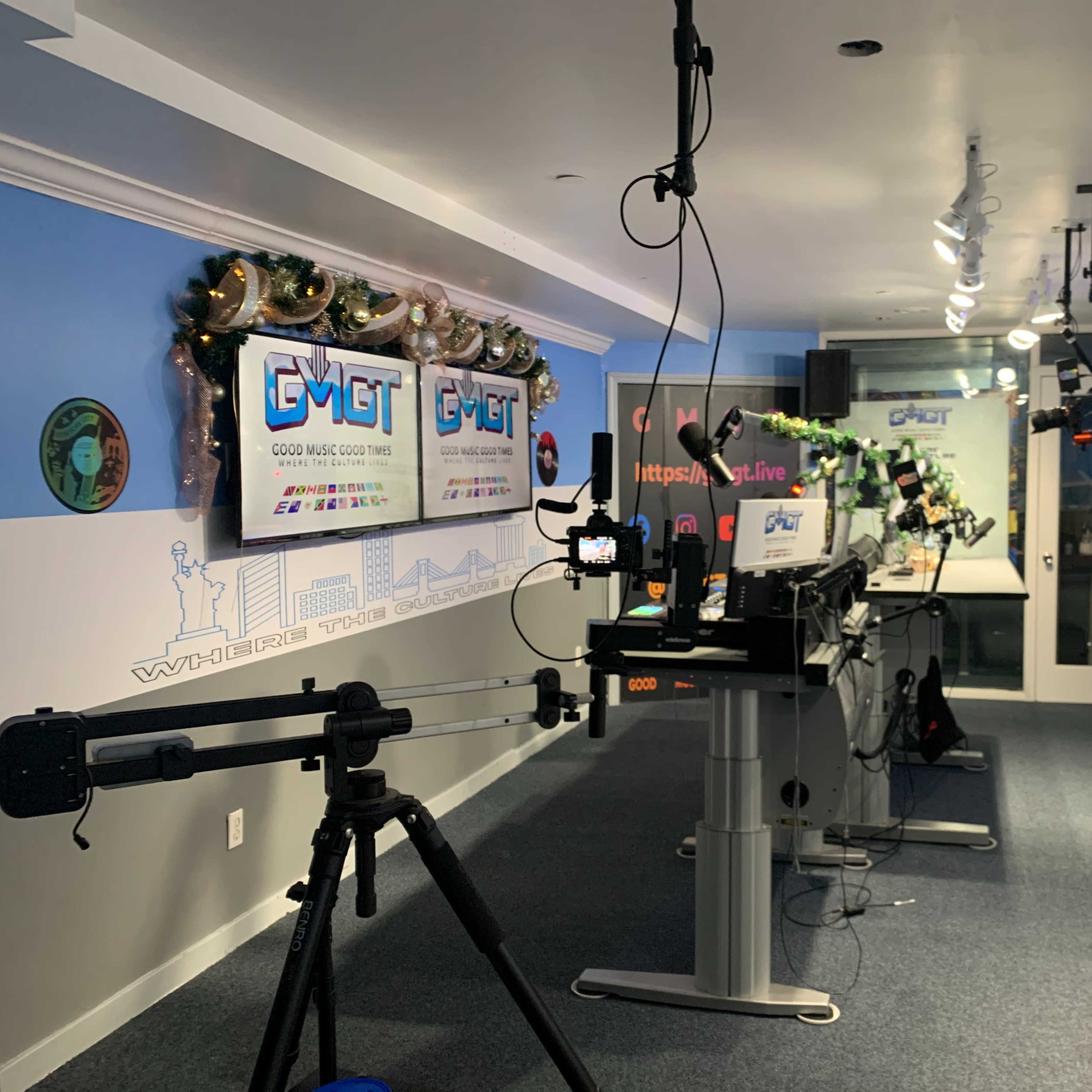 A brightly lit studio set up for live streaming, featuring multiple cameras, computer monitors, and promotional signage.