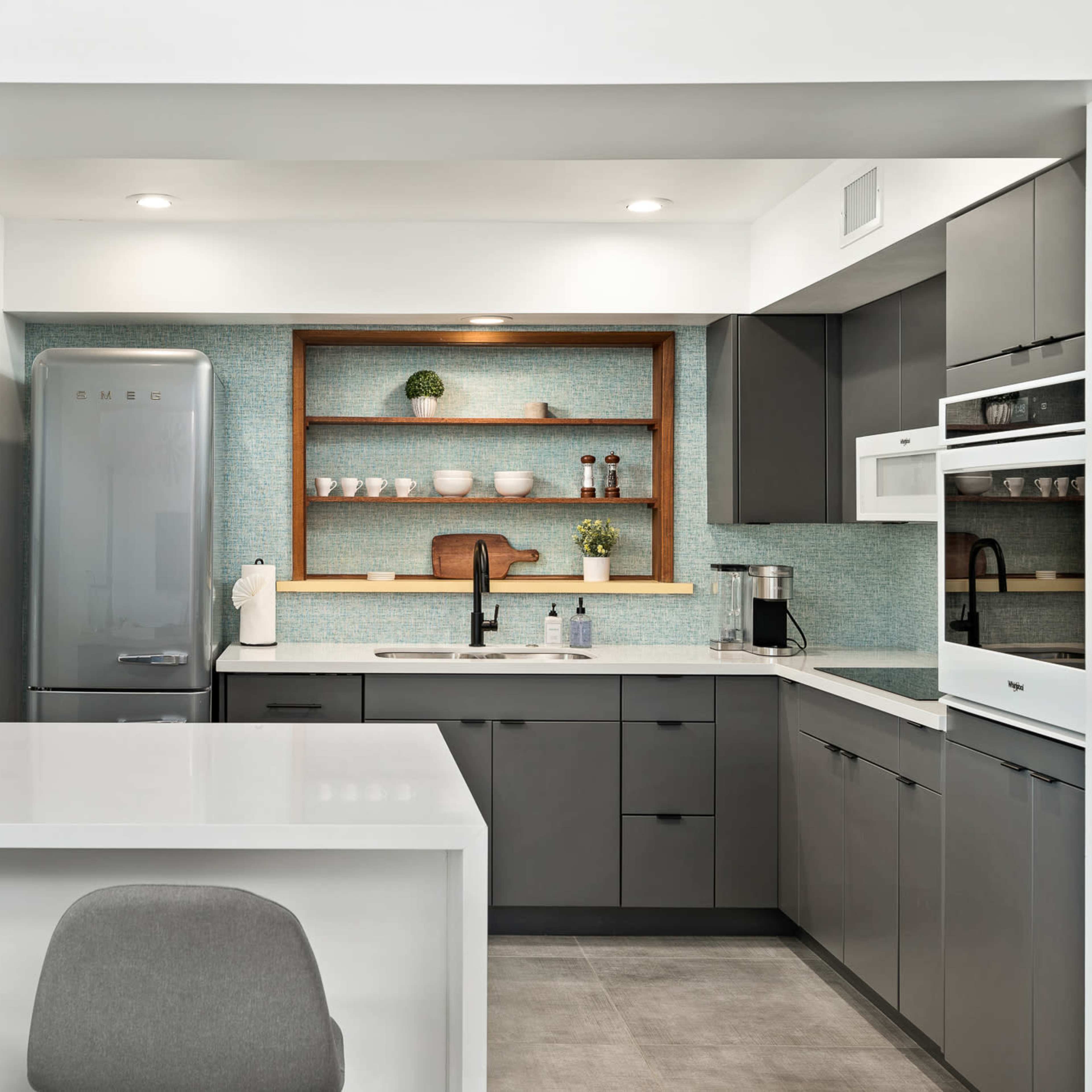 A modern kitchen with gray cabinetry, open shelves displaying dishware, and a light-colored countertop.