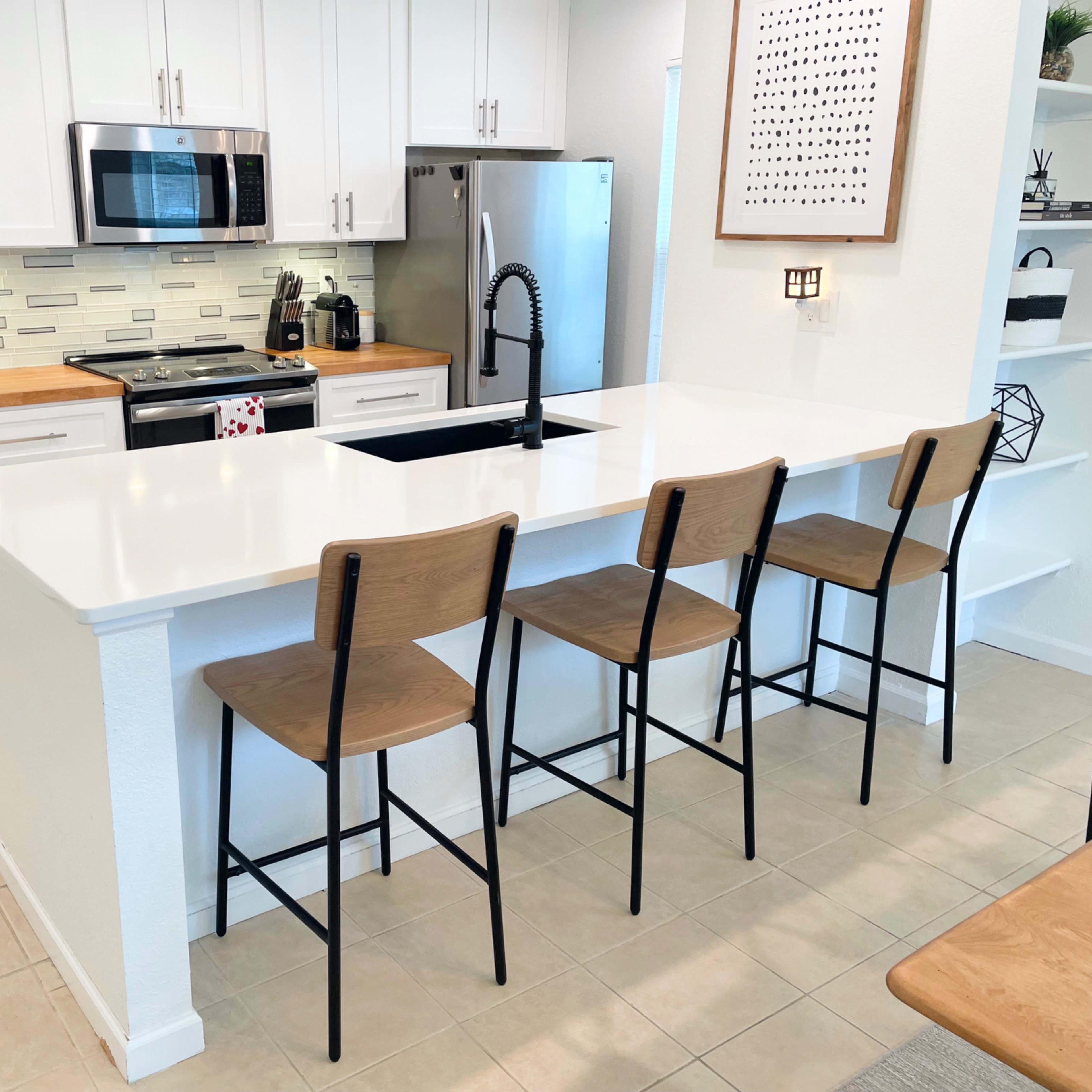 A modern kitchen features white cabinetry, stainless steel appliances, a large island with a sink, and four wooden bar stools.