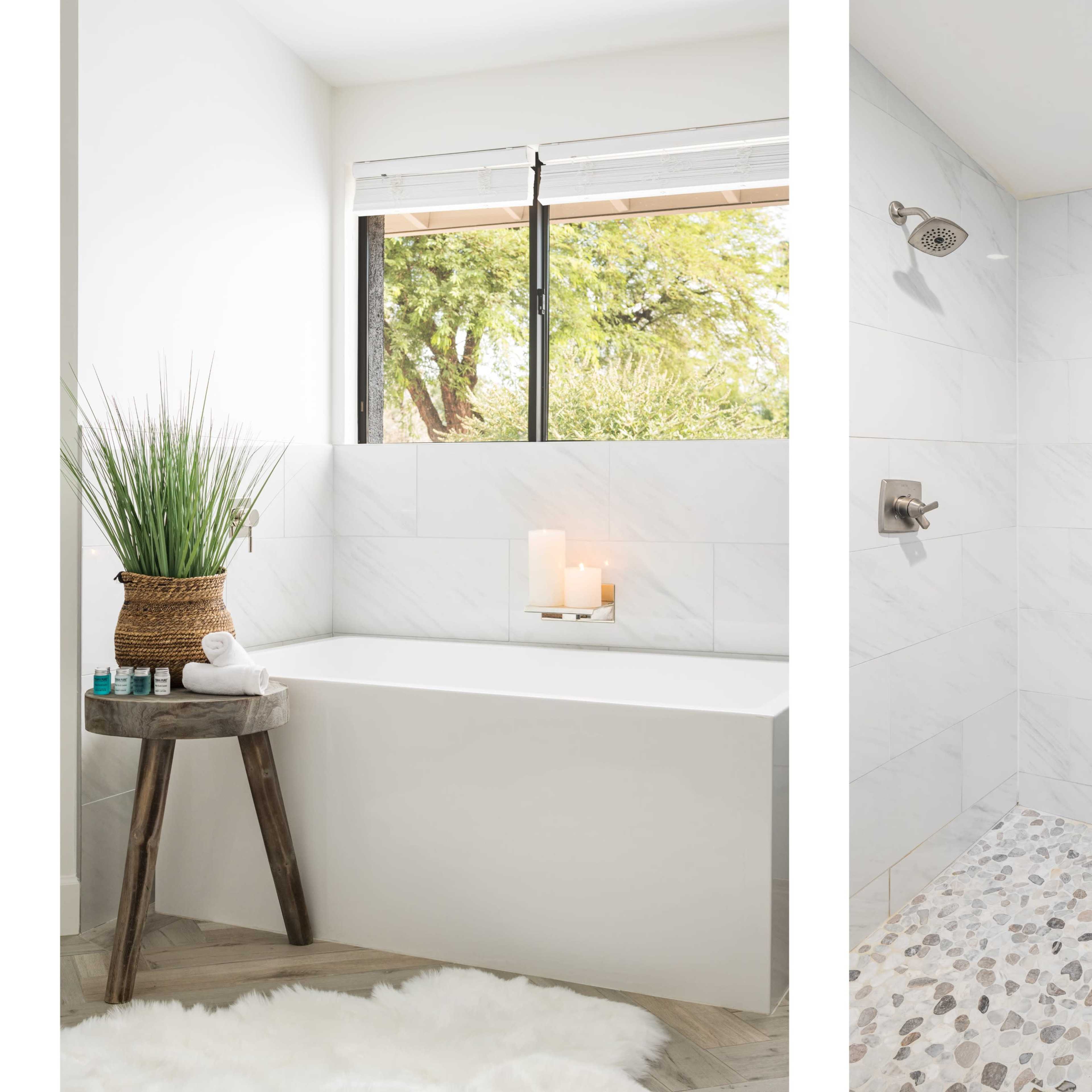 A modern bathroom featuring a freestanding bathtub beside a shower with pebble flooring and marble tile walls.