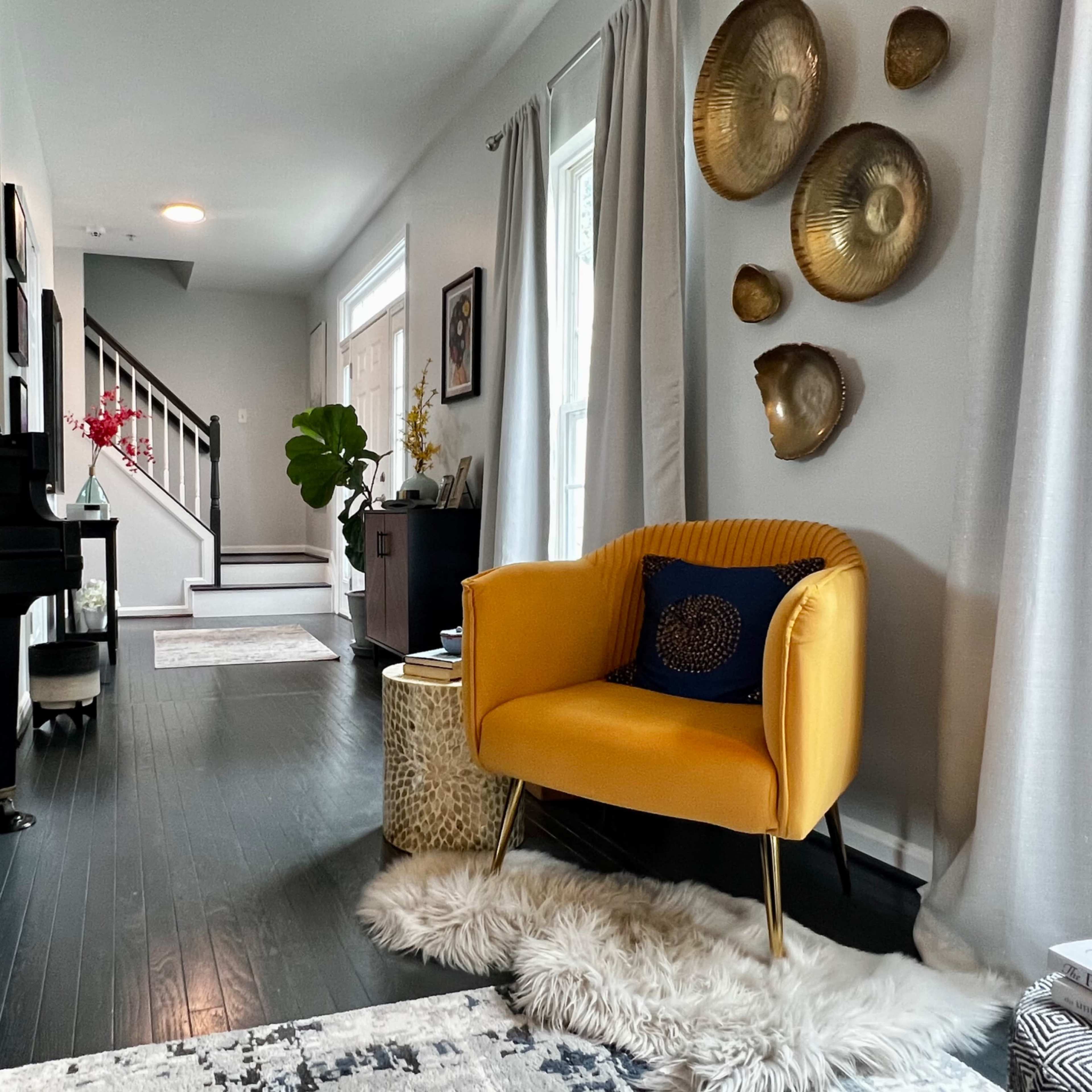 A modern living room features a black piano, a yellow armchair, and decorative wall plates, with a staircase in the background.
