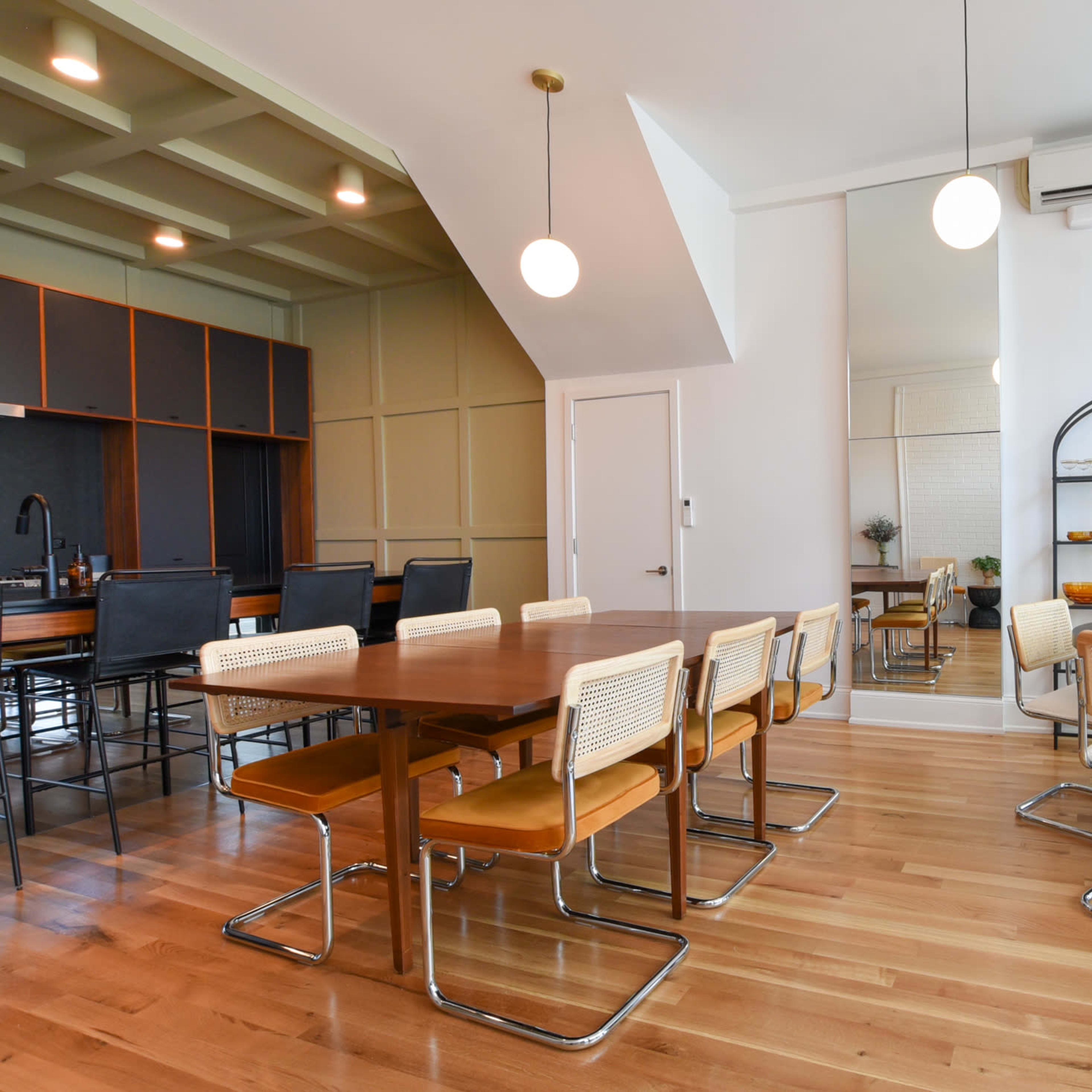 A modern dining area with a large wooden table and chairs, a smaller round table, and large windows allowing natural light to enter the space.