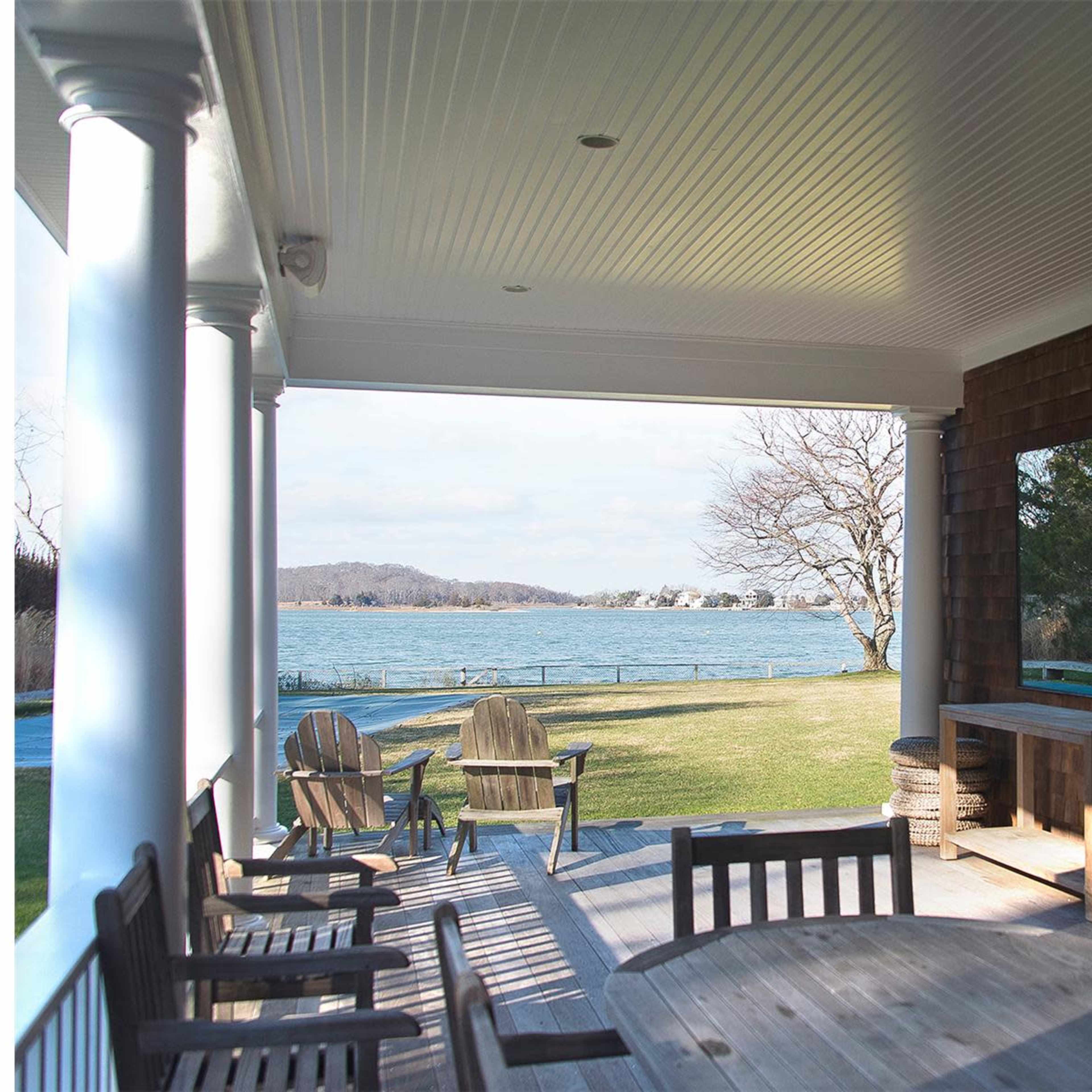 A porch with wooden furniture overlooks a lake, framed by columns and a brick fireplace.