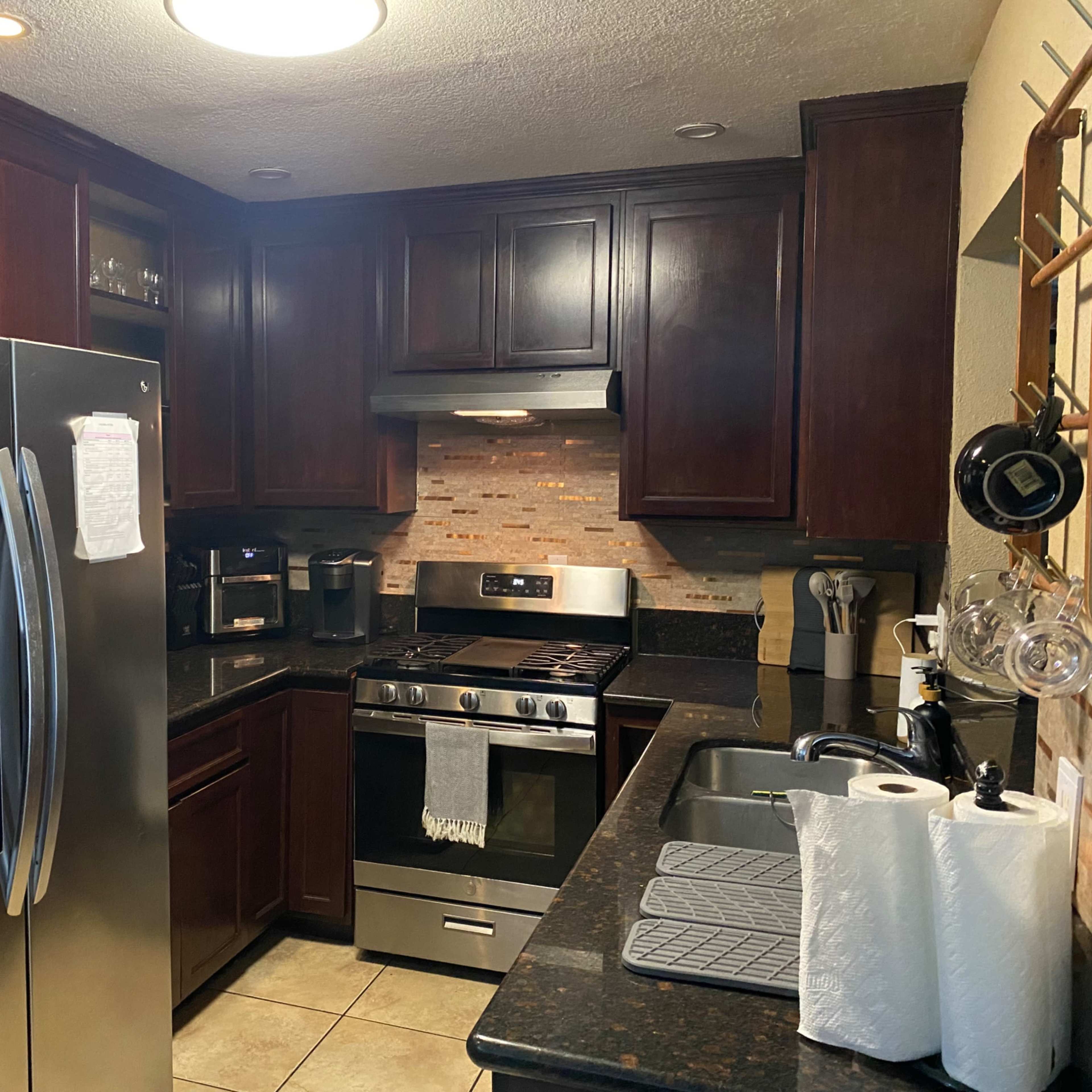 A modern kitchen featuring dark wood cabinets, stainless steel appliances, and a granite countertop with a sink.