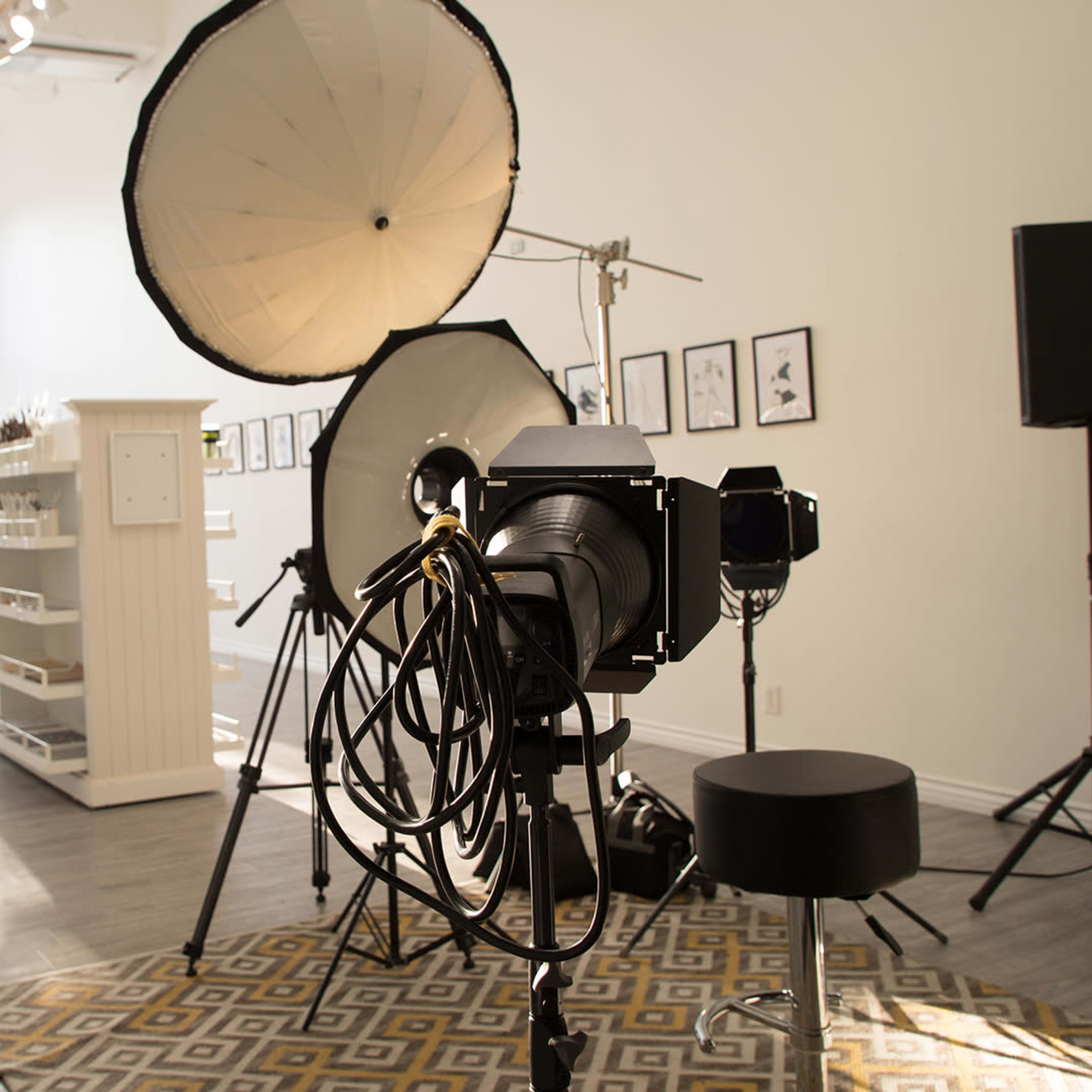 A photography studio setup with large light sources, a camera on a tripod, and a patterned rug on the floor.