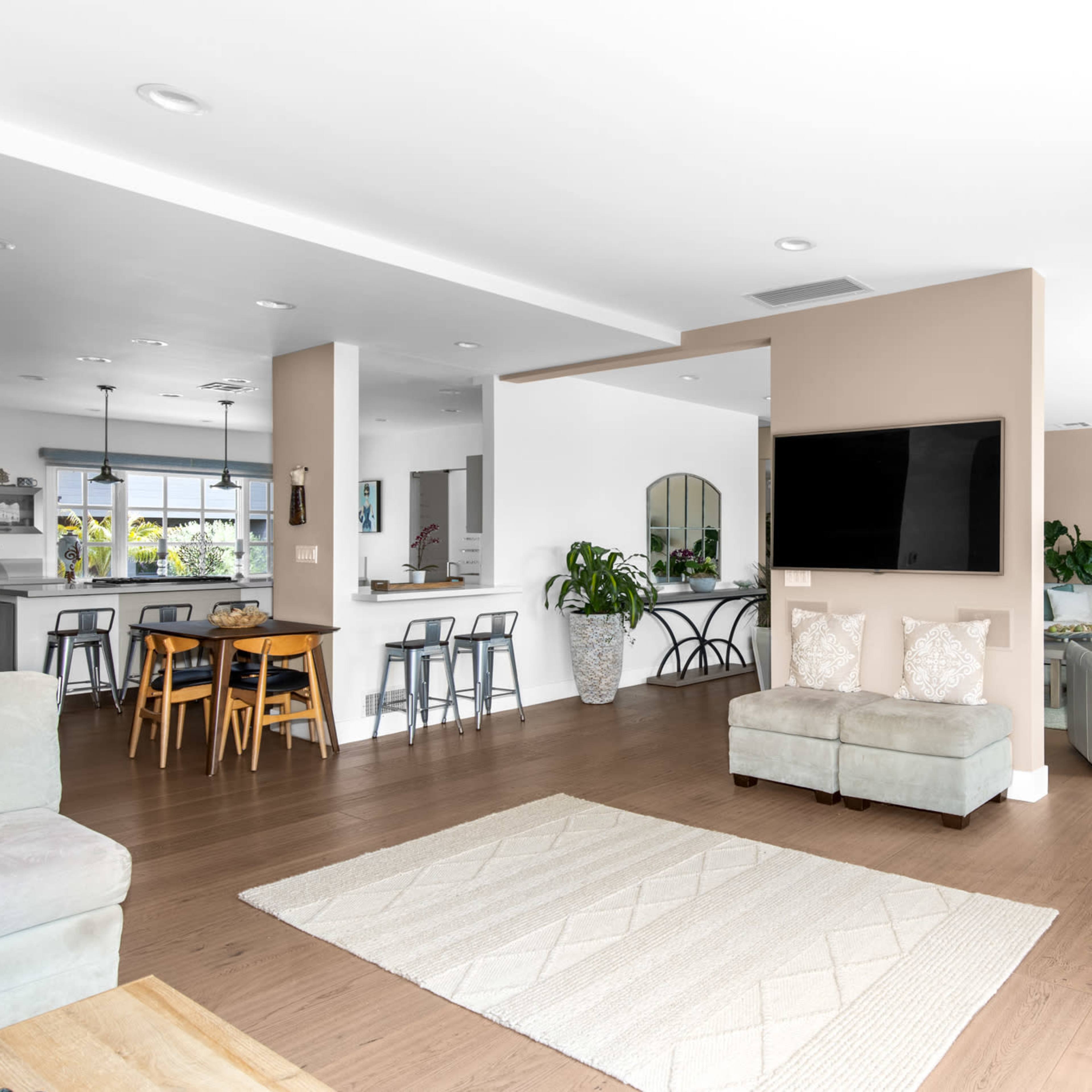 A modern open-concept living space that includes a seating area, dining table, kitchen bar, and large windows with plants integrated into the decor.