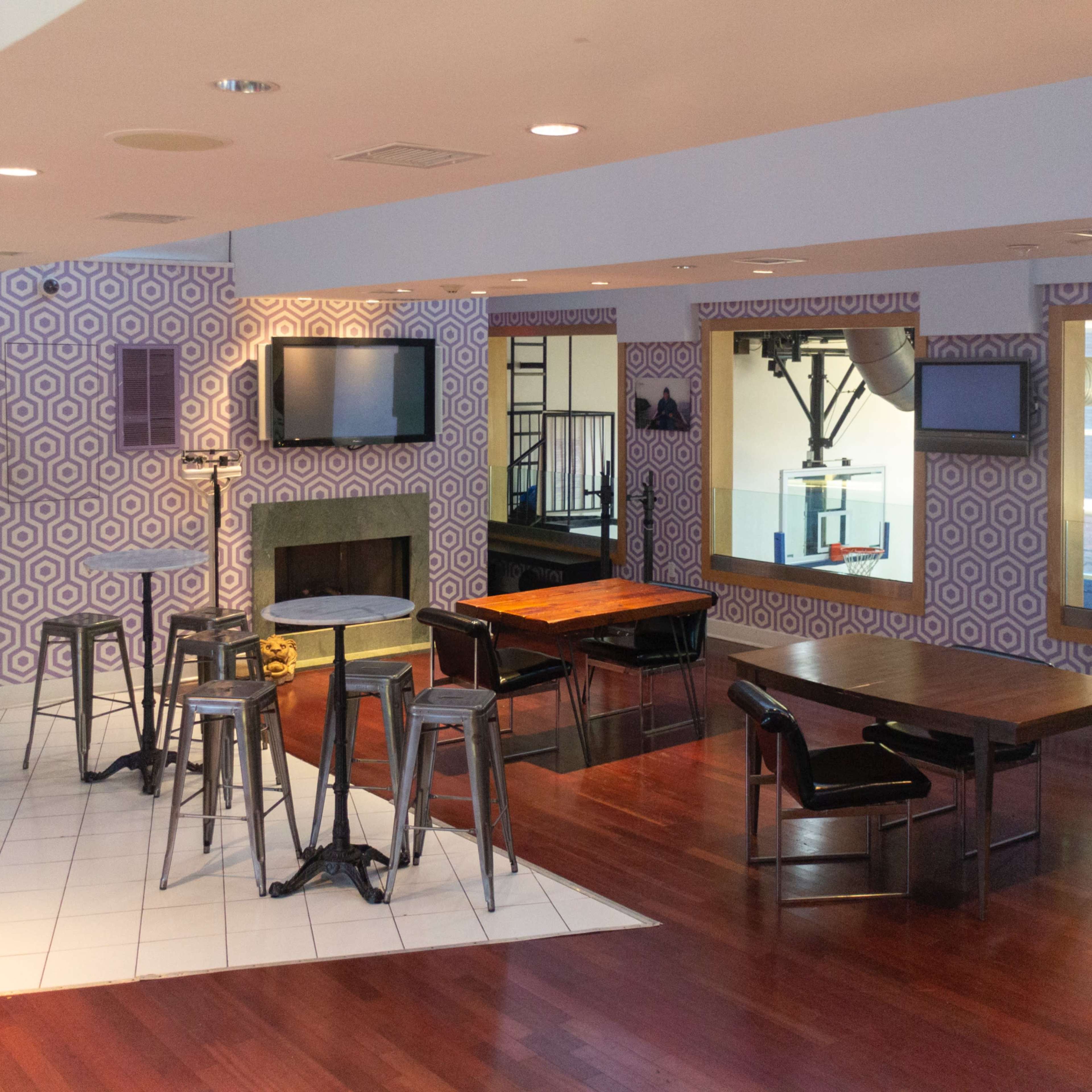 A modern open-concept lounge area featuring a kitchen with appliances, multiple tables with chairs, and distinctive patterned wallpaper.